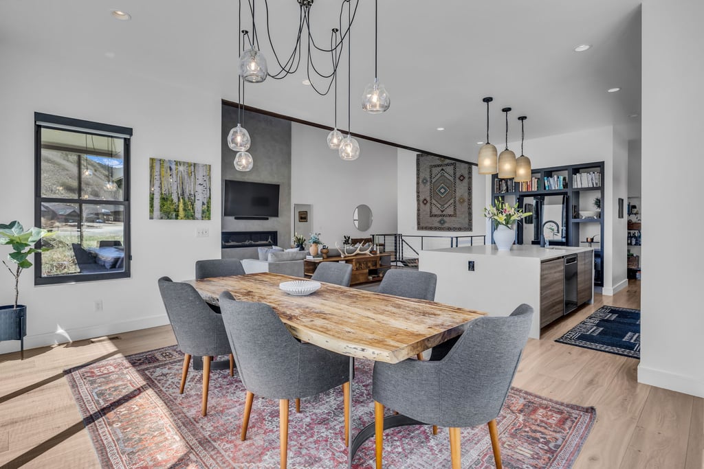 Open-concept living area featuring a large dining table with seating, light wood-finish flooring, and a modern kitchen island with pendant lighting