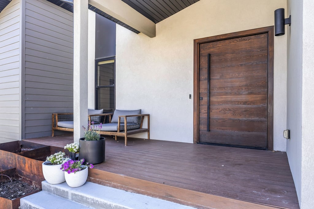 Inviting porch entry featuring a contemporary wood-finish door with a long black pull handle, durable composite decking, and a textured stucco exterior