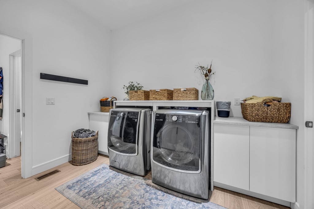 Dedicated laundry area featuring modern front-loading appliances, white cabinetry, and a stone-finish countertop