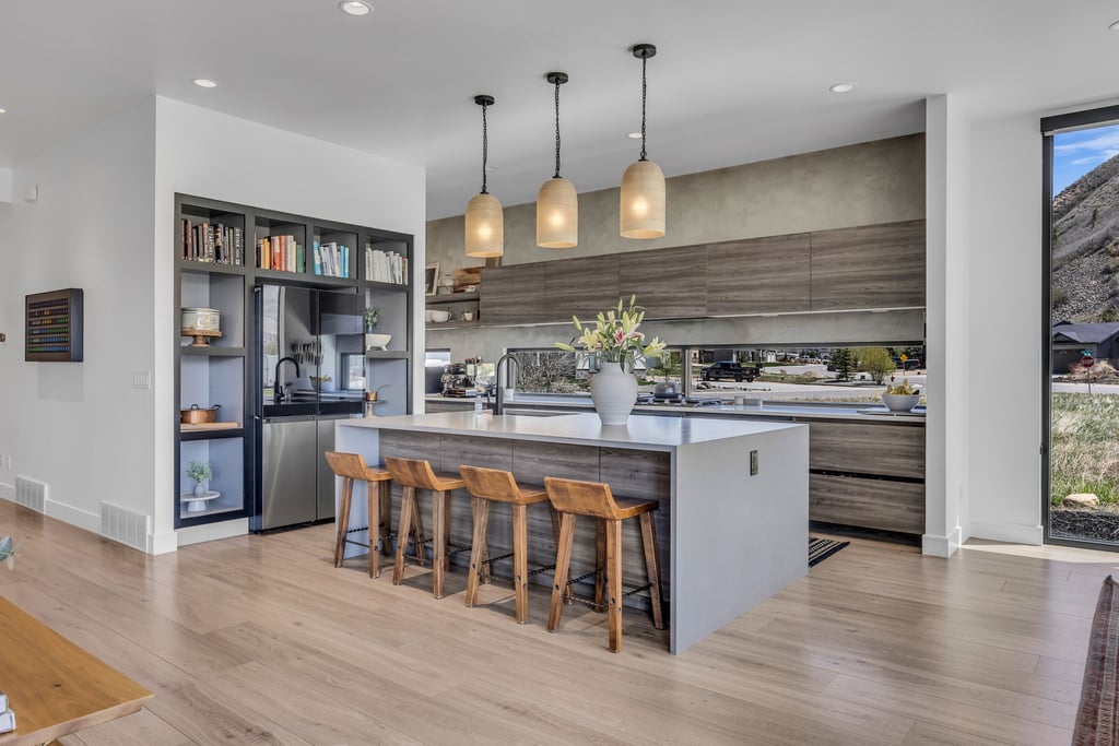 Modern kitchen featuring a large central island with seating, pendant lighting, wood-finish flooring, built-in shelving, and stainless steel appliances