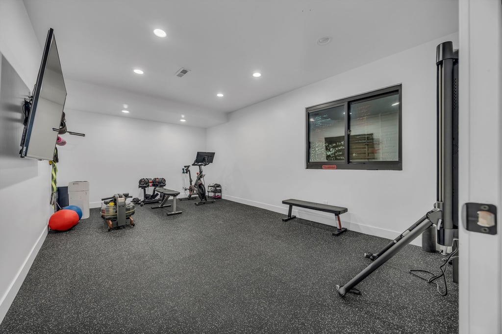 Dedicated fitness space featuring resilient black flooring, recessed ceiling lighting, a large wall-mounted display, and a modern window