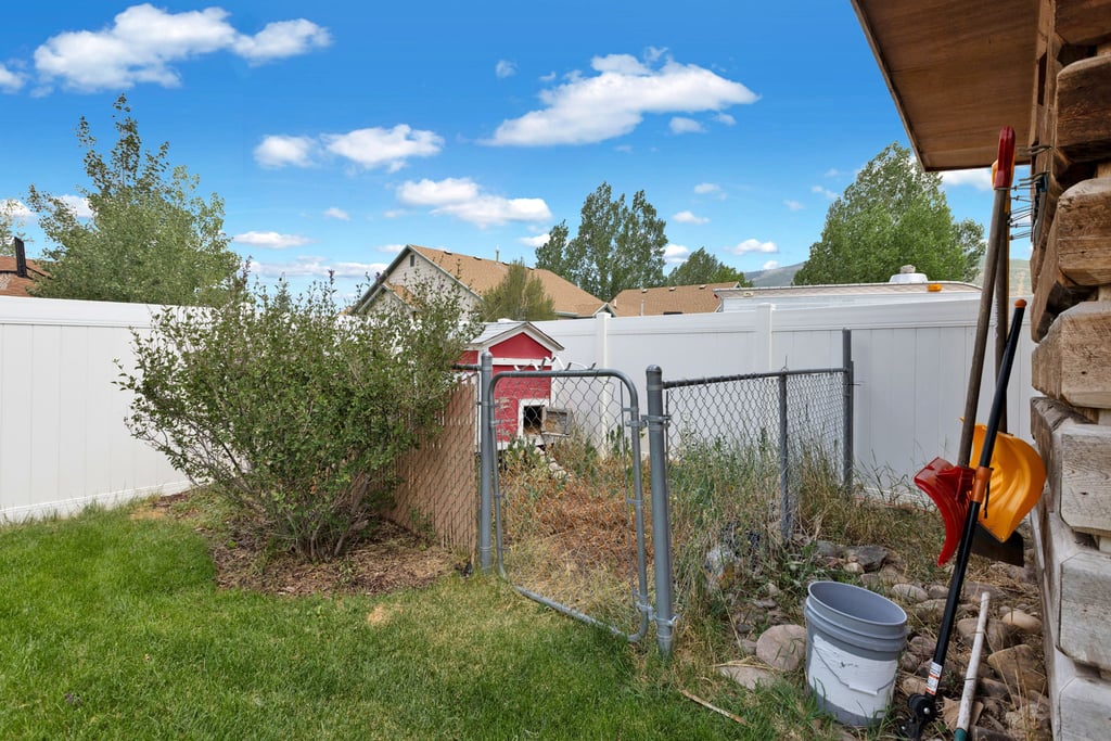 Fenced backyard area featuring a chain-link fence, mature shrubbery, and a white privacy fence