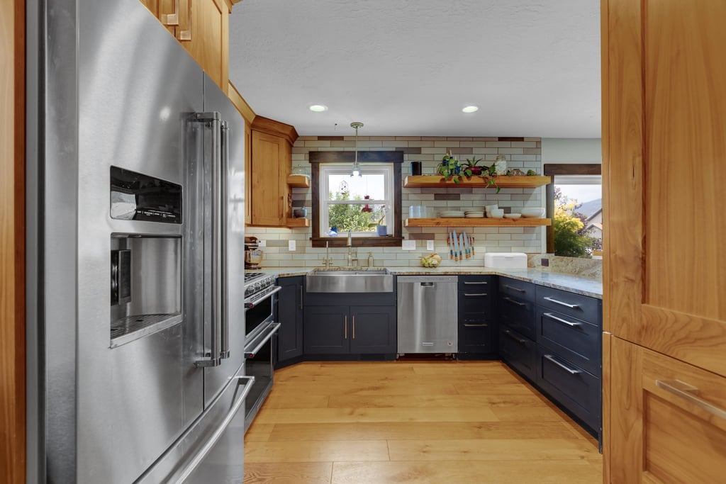 Modern kitchen featuring stainless steel appliances, wood-finish flooring, dark blue base cabinetry, light wood upper cabinetry, and open shelving