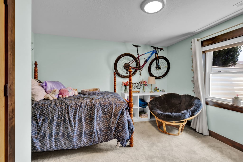 Bedroom with light blue walls, light-colored carpet flooring, and a large window featuring wood trim
