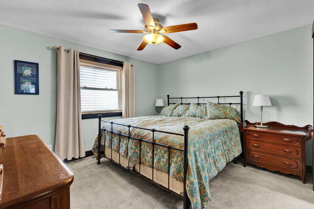 Comfortable bedroom featuring a ceiling fan with integrated lighting, a window with blinds and drapes, and plush carpet flooring