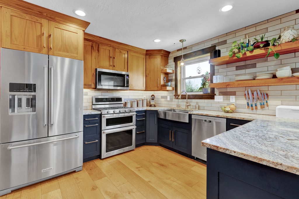 Contemporary kitchen featuring stainless steel appliances, two-tone cabinetry, wood-finish flooring, light-toned countertops, and a subway tile backsplash
