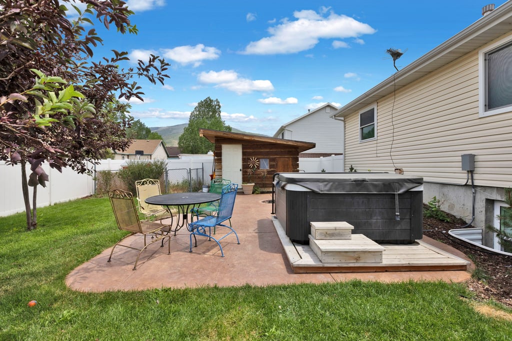 Expansive backyard featuring a hot tub with dedicated wood platform, a concrete patio, and a detached shed with a lean-to roof