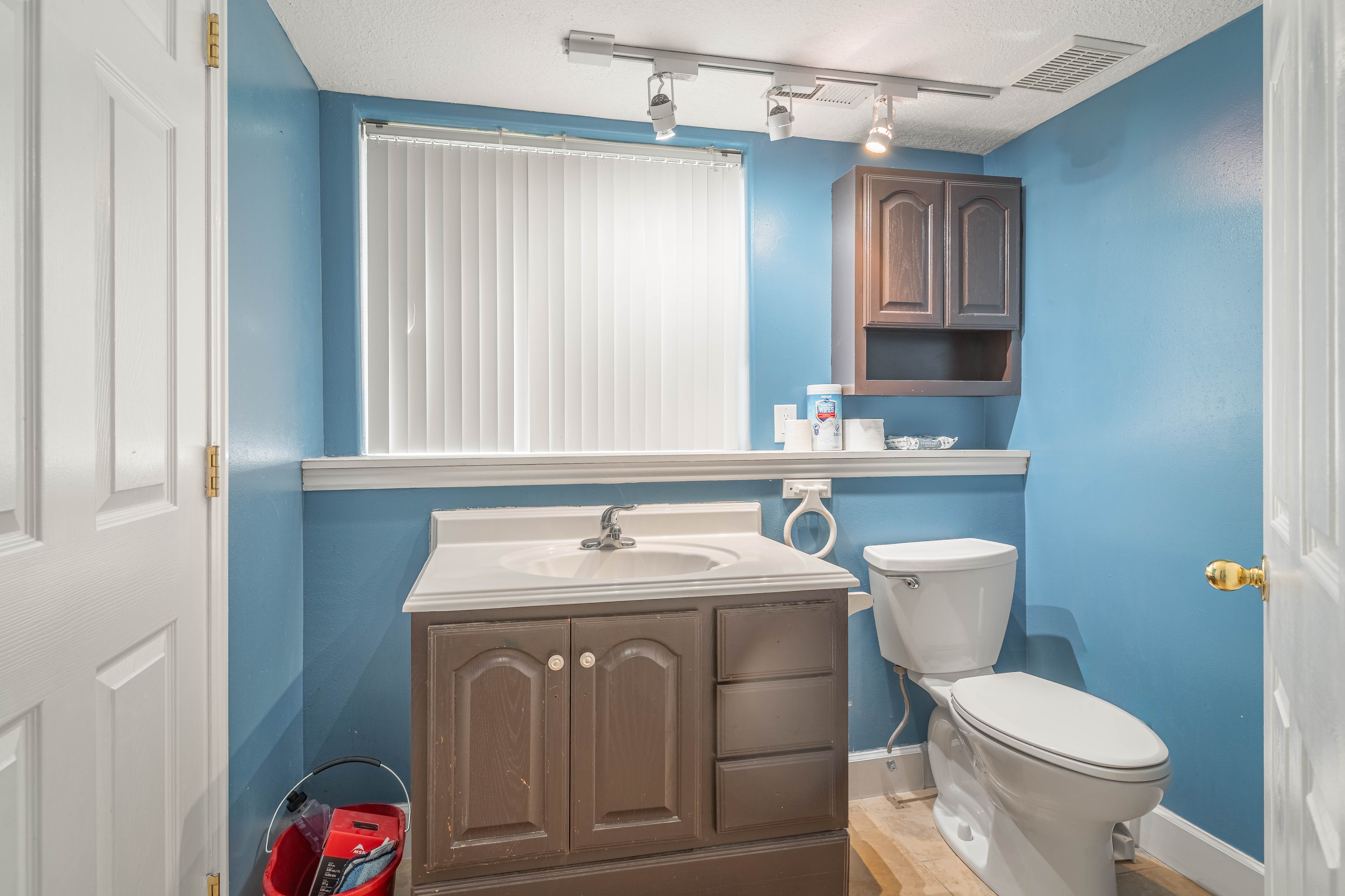 Bathroom featuring a wood-finish vanity with an integrated sink, white countertop, and track lighting