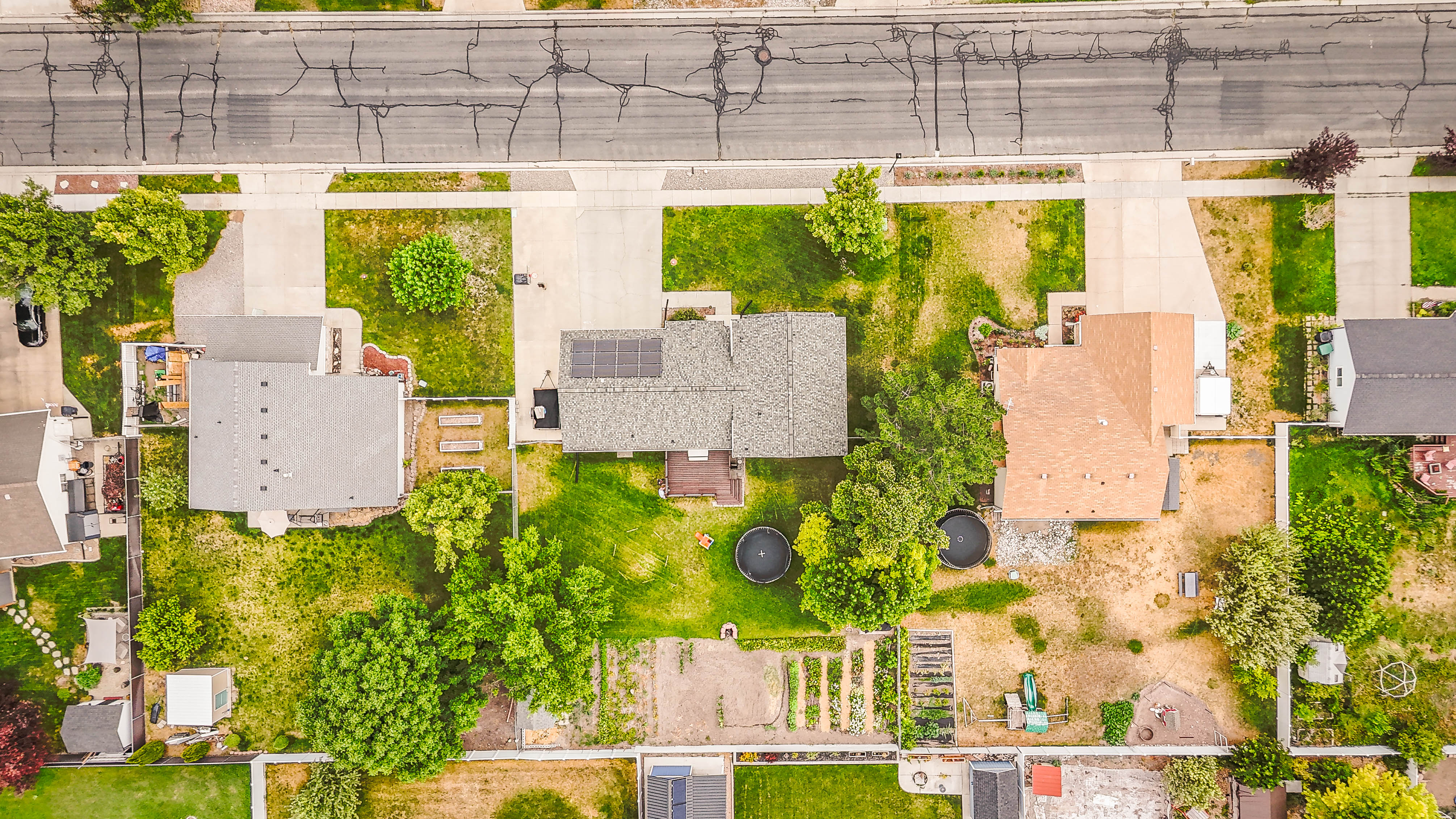Aerial view showcasing three residential properties with paved driveways and varied landscaping