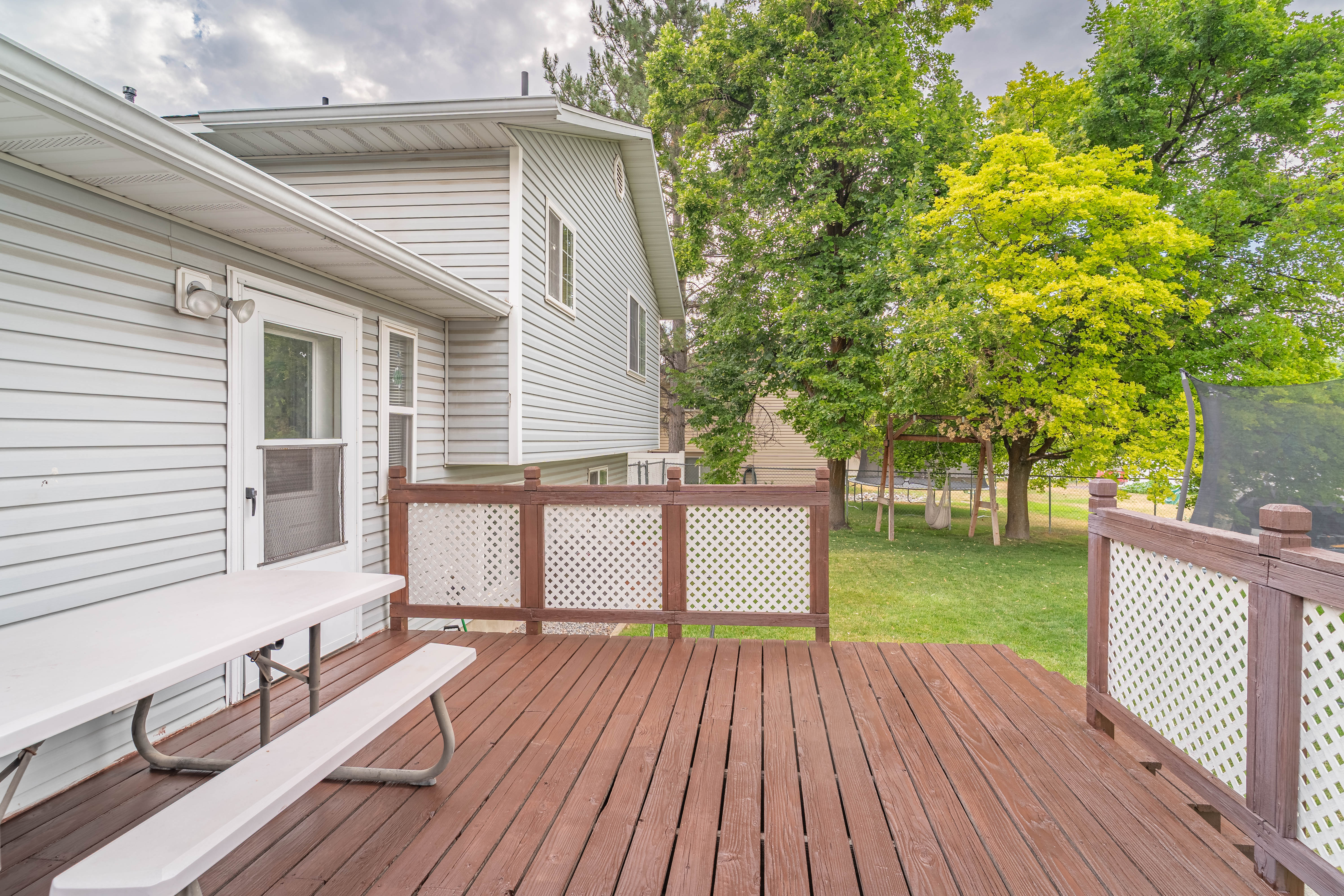 Wood-finish deck with decorative lattice railing, providing outdoor access from the light gray siding exterior