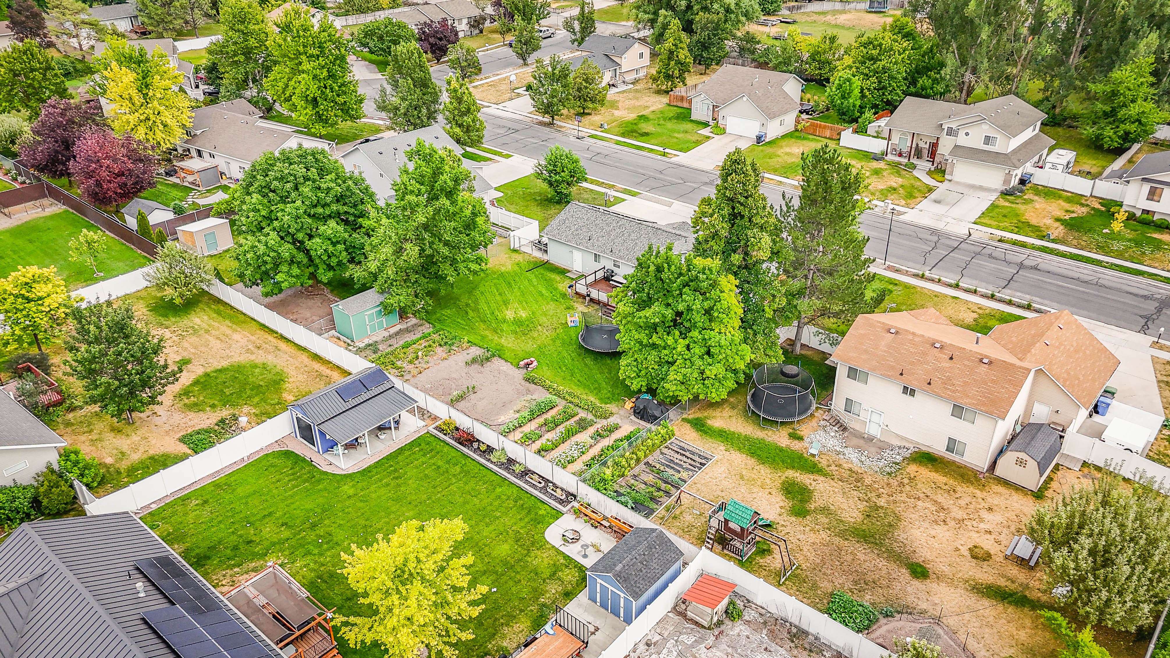 Expansive property featuring a meticulously maintained lawn, established garden beds, white perimeter fencing, and mature trees
