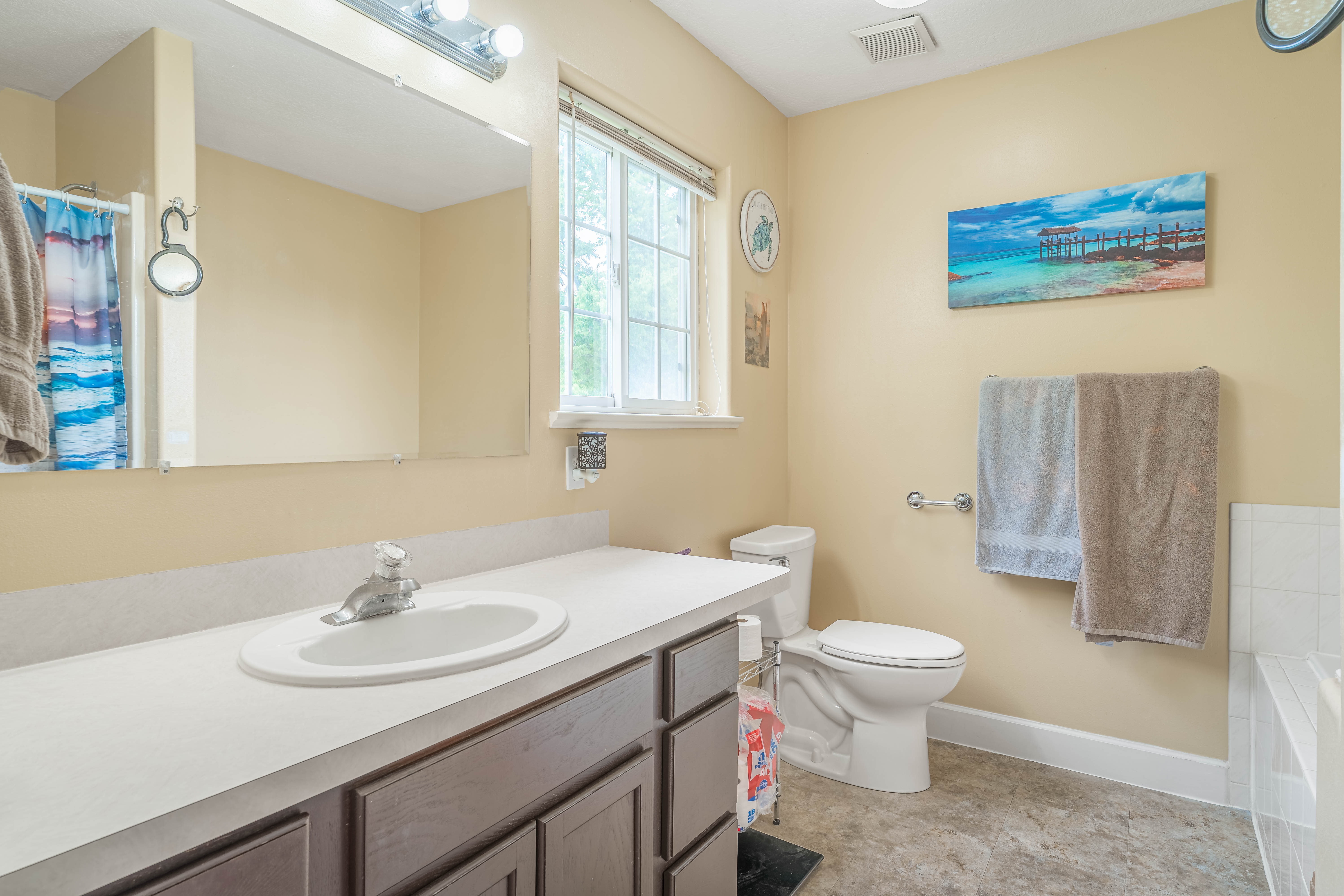 Bathroom featuring a dark wood-finish vanity with an integrated sink, a large wall-mounted mirror, and a window with natural light