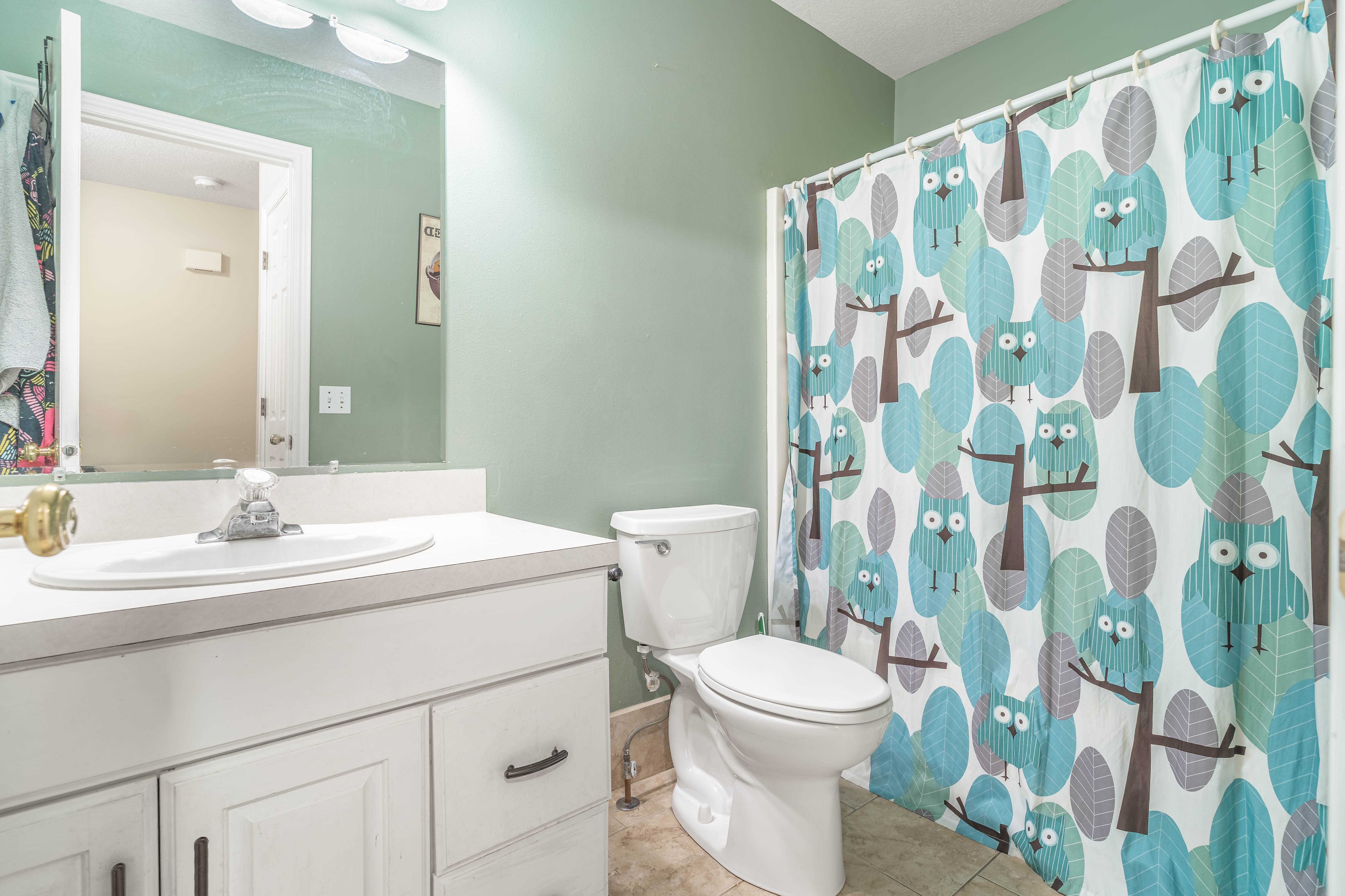 Bathroom featuring a white vanity with integrated sink, chrome faucet, wall-mounted mirror, and white toilet