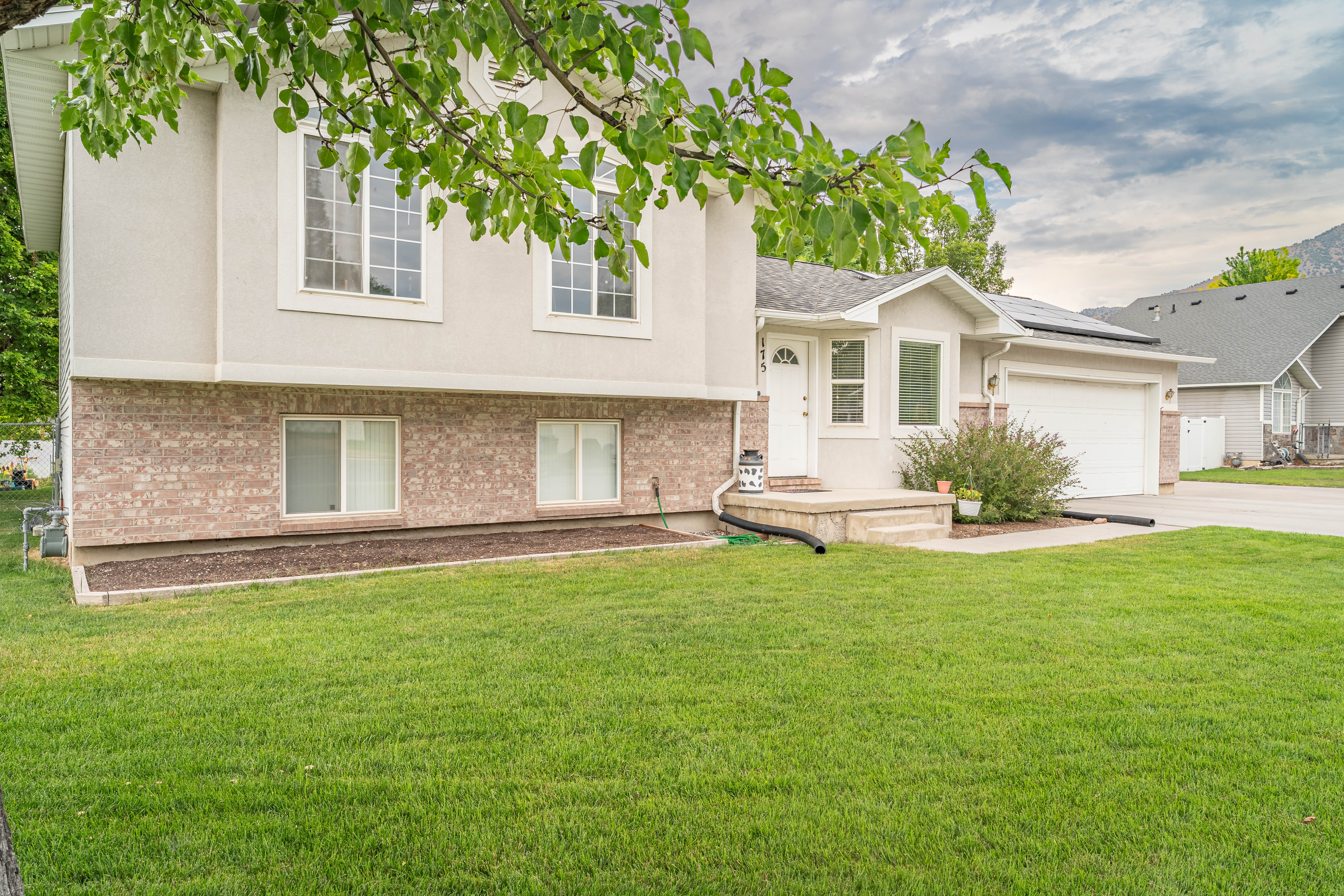 Two-story residence featuring a brick and stucco facade, an attached garage, a covered front entry, and a manicured lawn