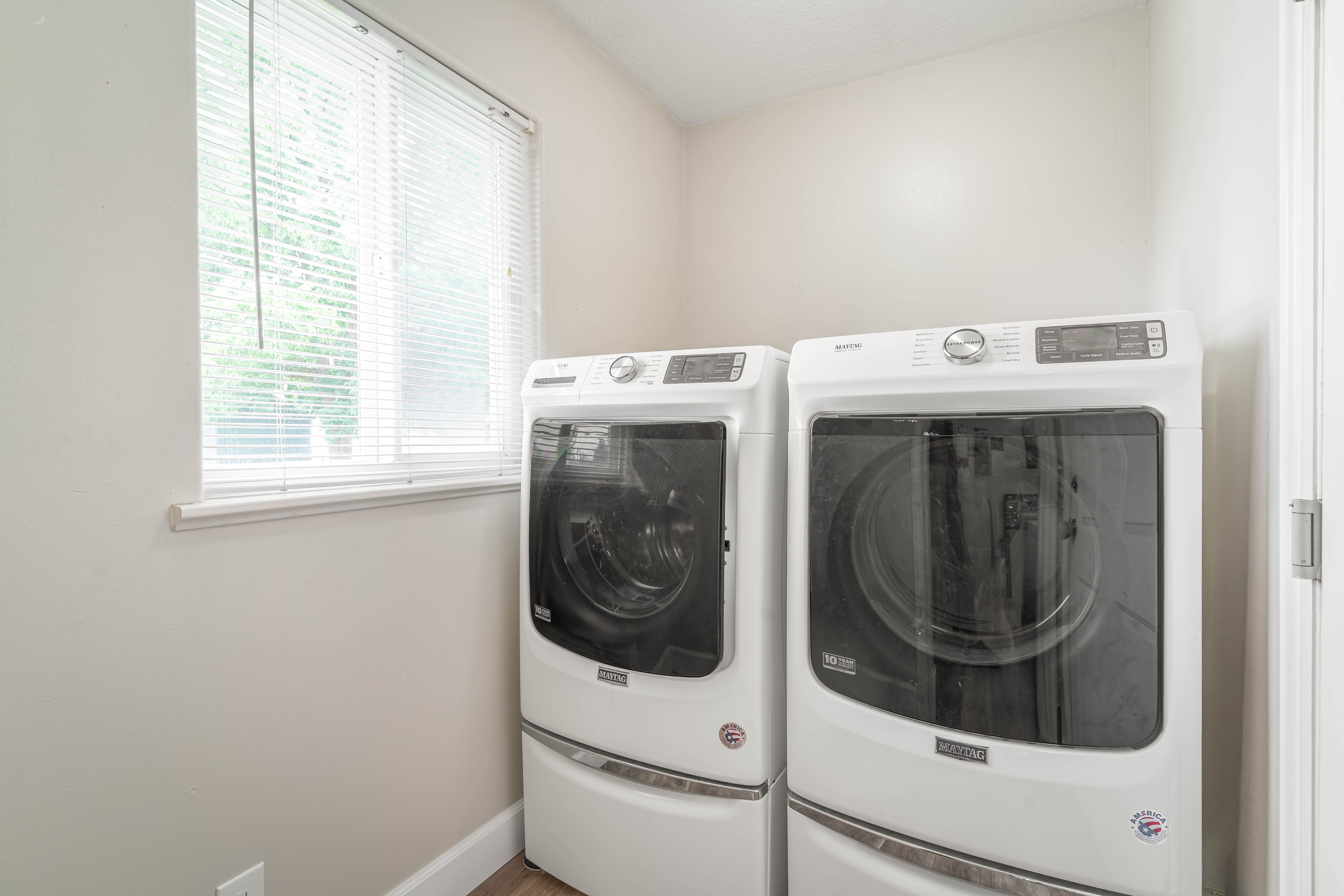 Dedicated laundry area featuring a large window with blinds, light neutral wall tones, and wood-finish flooring