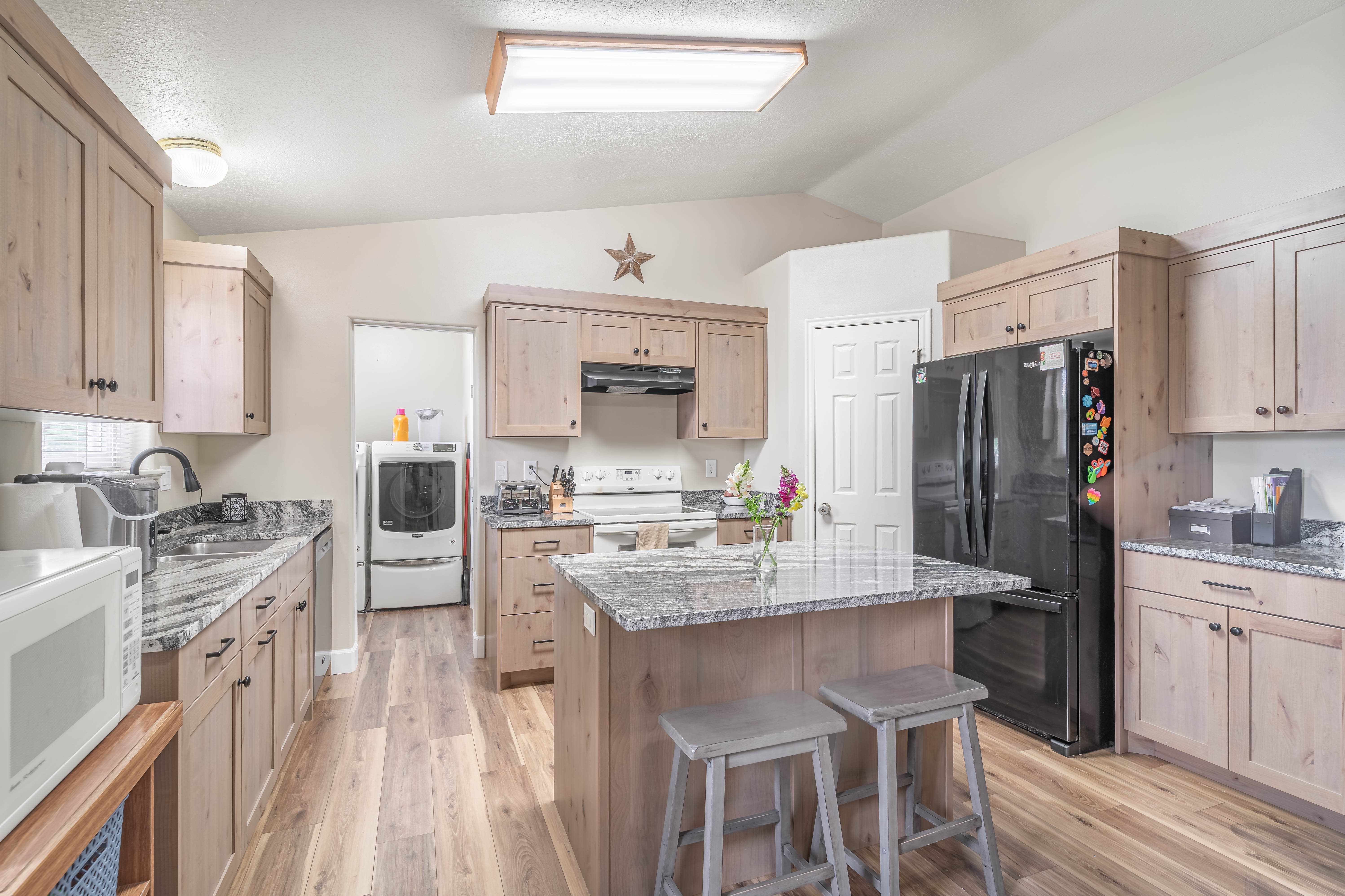 Kitchen featuring light wood-finish cabinetry, granite countertops, wood-finish flooring, and a central island with countertop seating