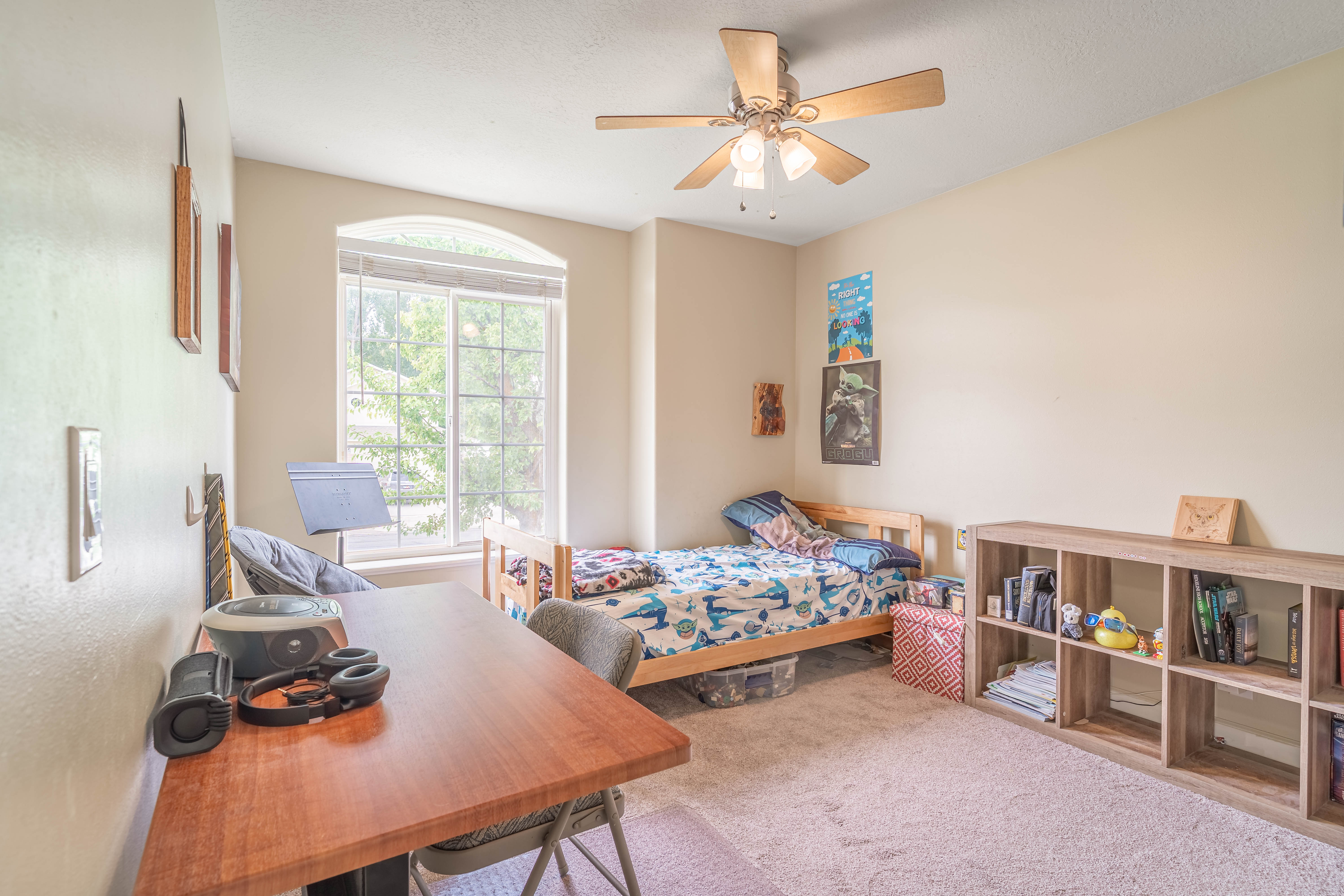 Light-filled room featuring neutral wall tones, arched window, and a ceiling fan with integrated lighting
