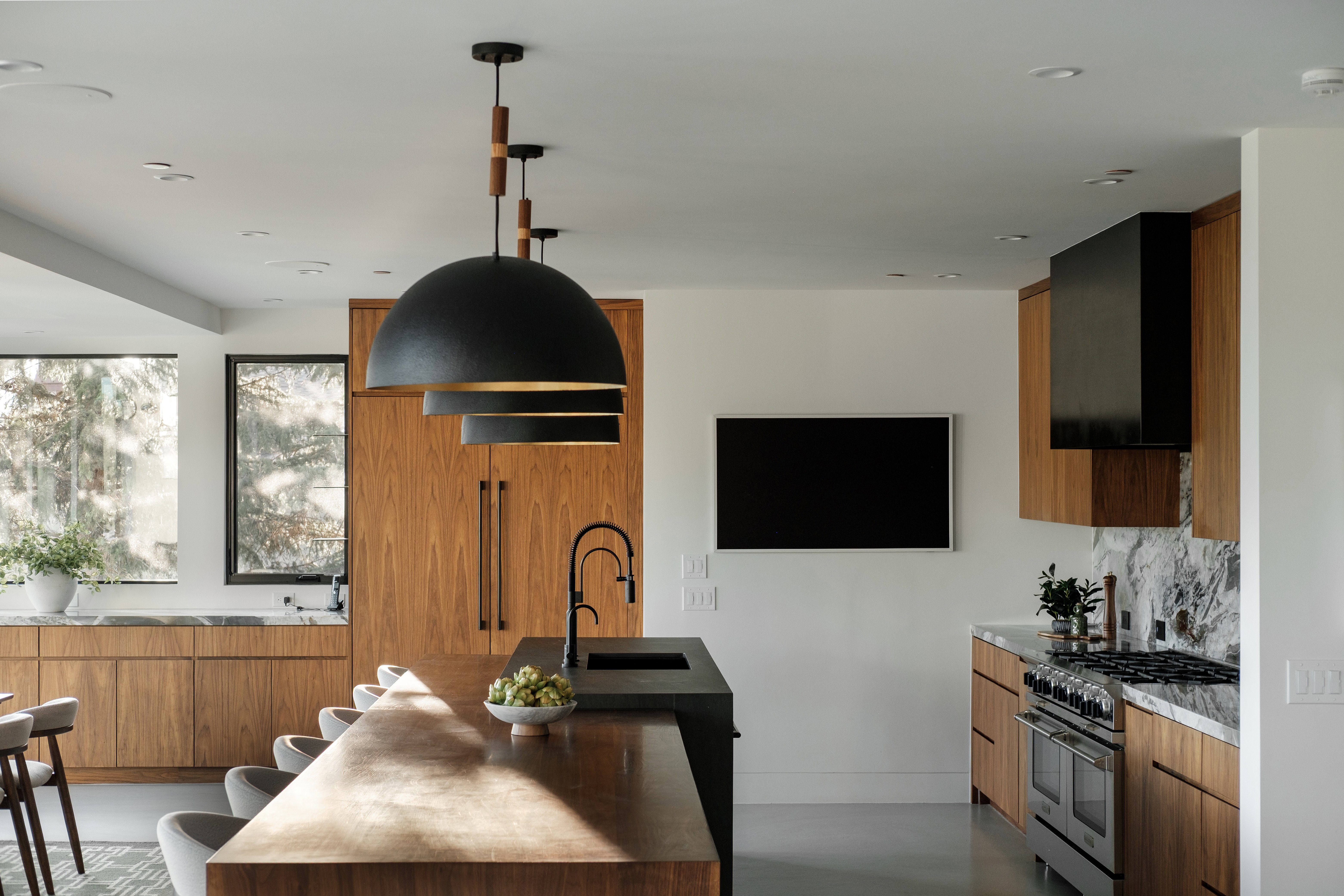 Contemporary kitchen featuring a large wood-finish island, black pendant lighting, and stainless steel appliances