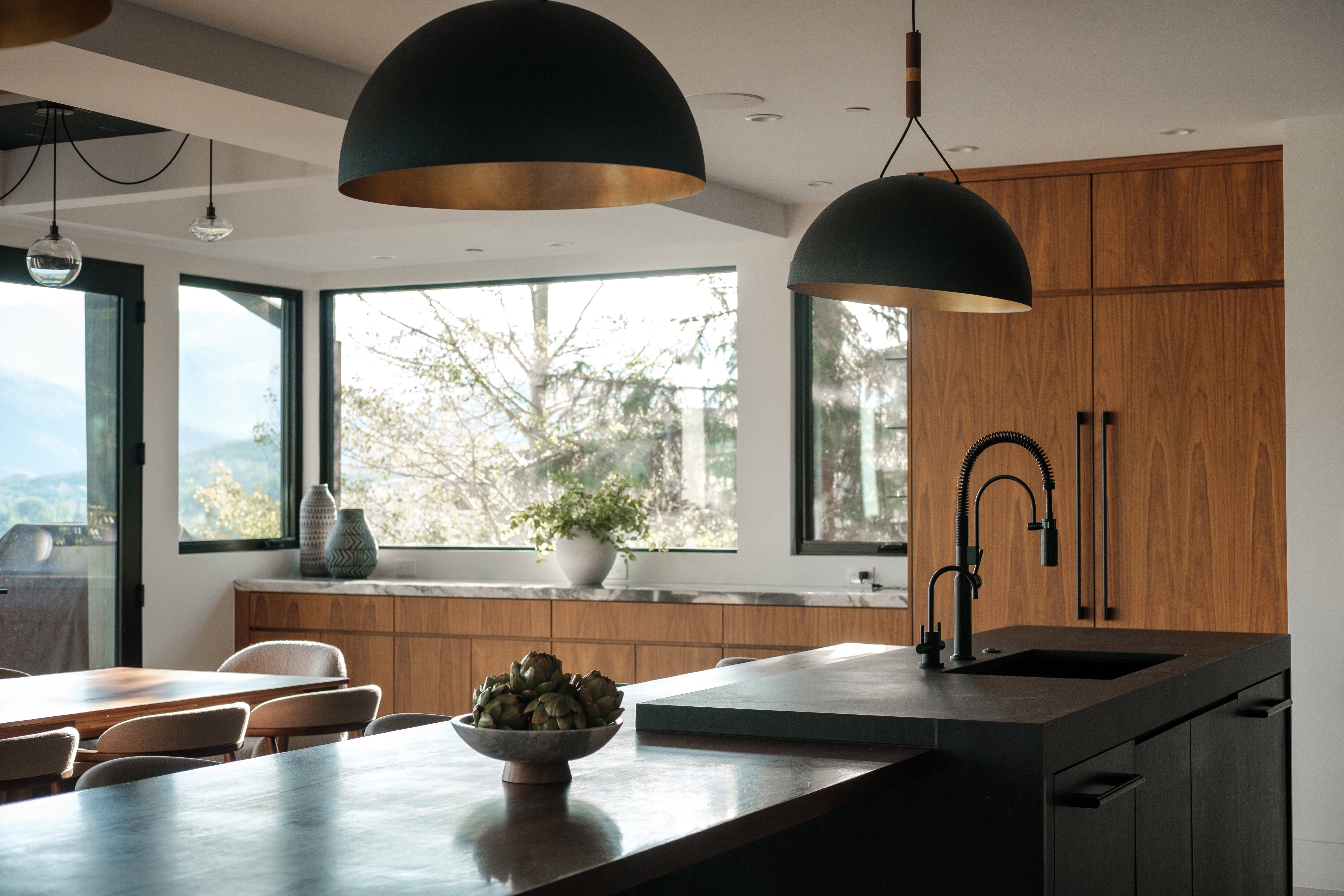 Modern kitchen featuring a dark countertop island with an integrated sink and matte black faucet, wood-finish cabinetry, and contemporary pendant lighting