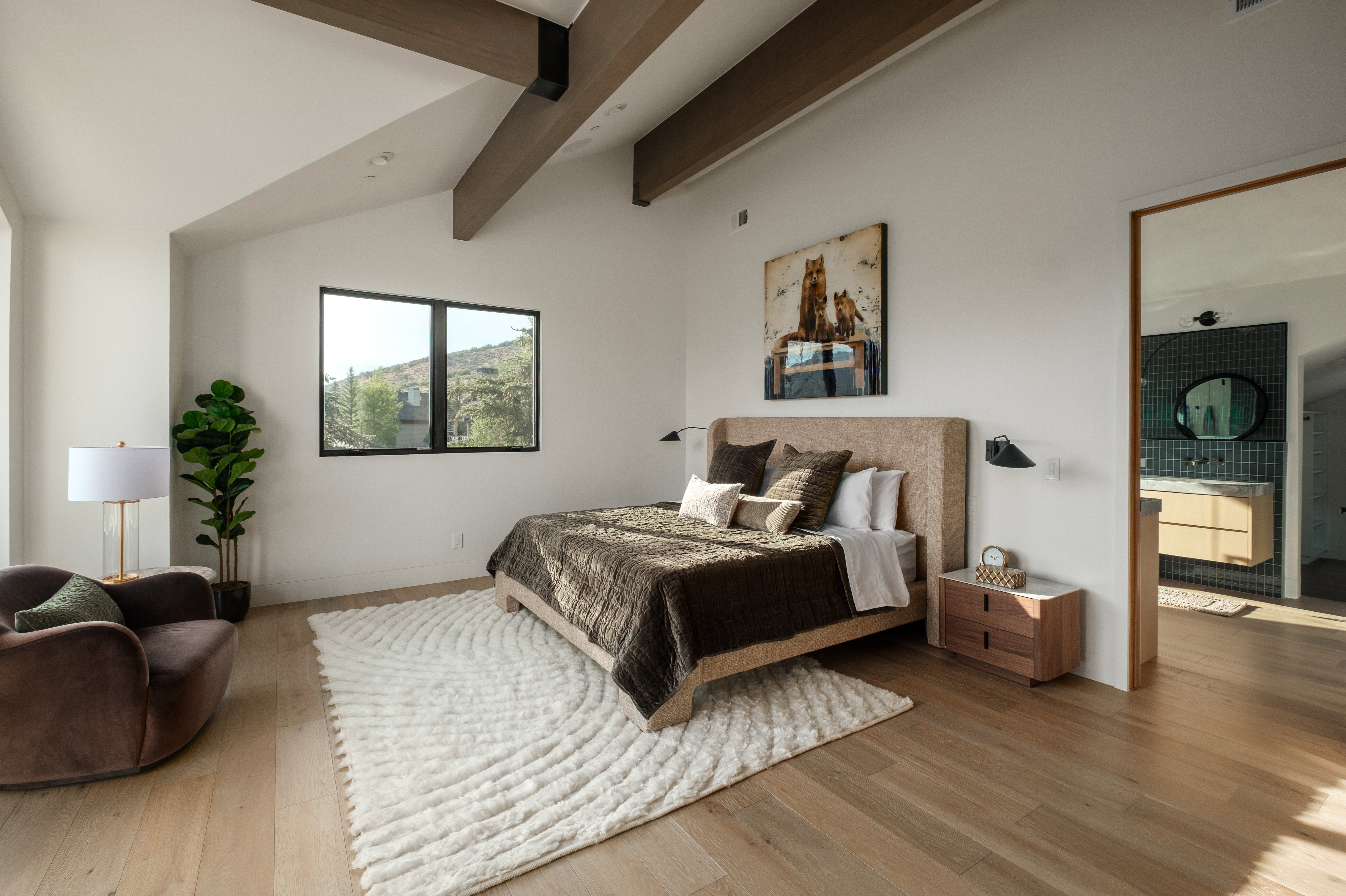 Spacious bedroom featuring vaulted ceilings with exposed wood beams, light wood-finish flooring, and a large window