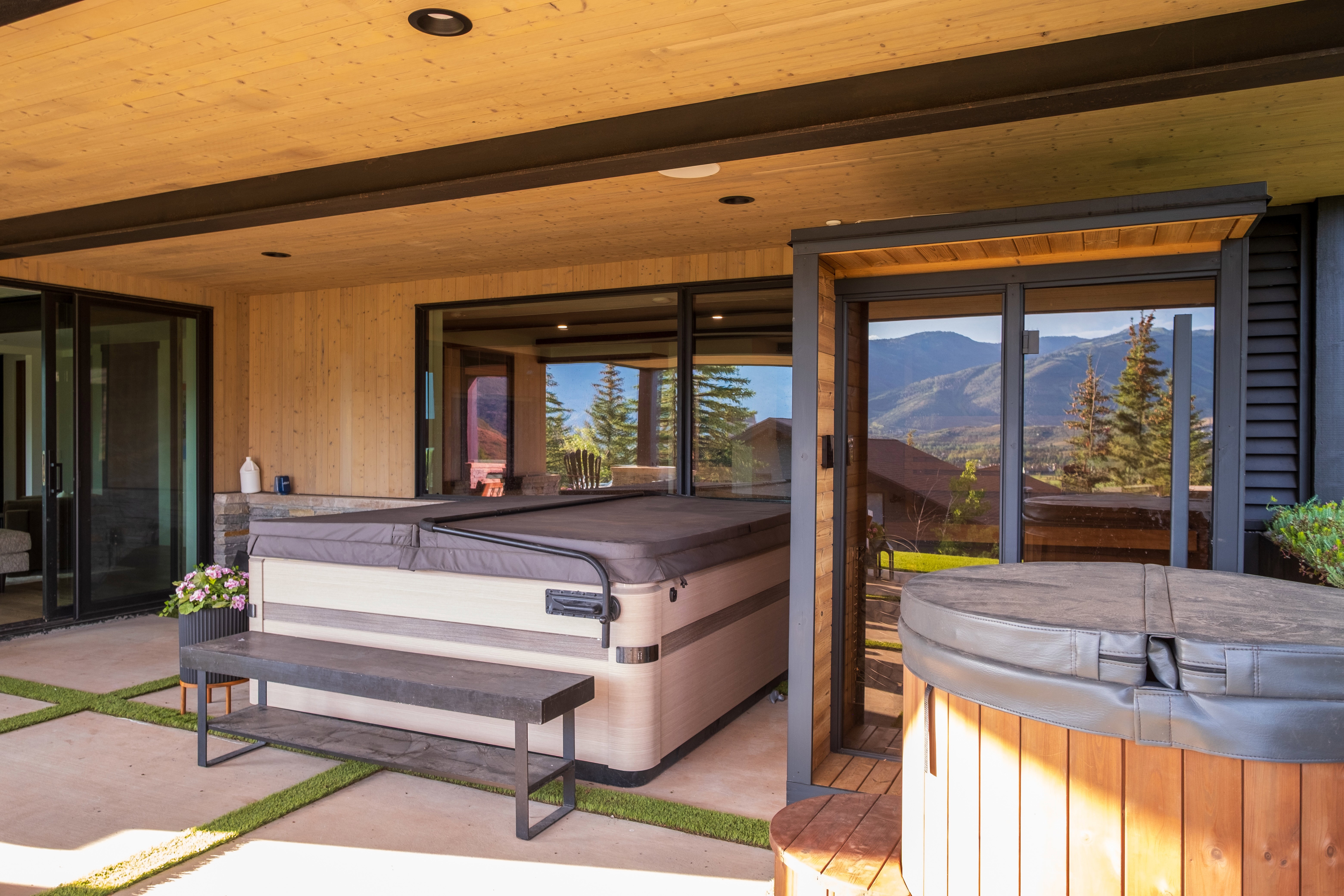 Covered outdoor patio featuring two hot tubs, concrete flooring with artificial turf accents, and wood-finish siding