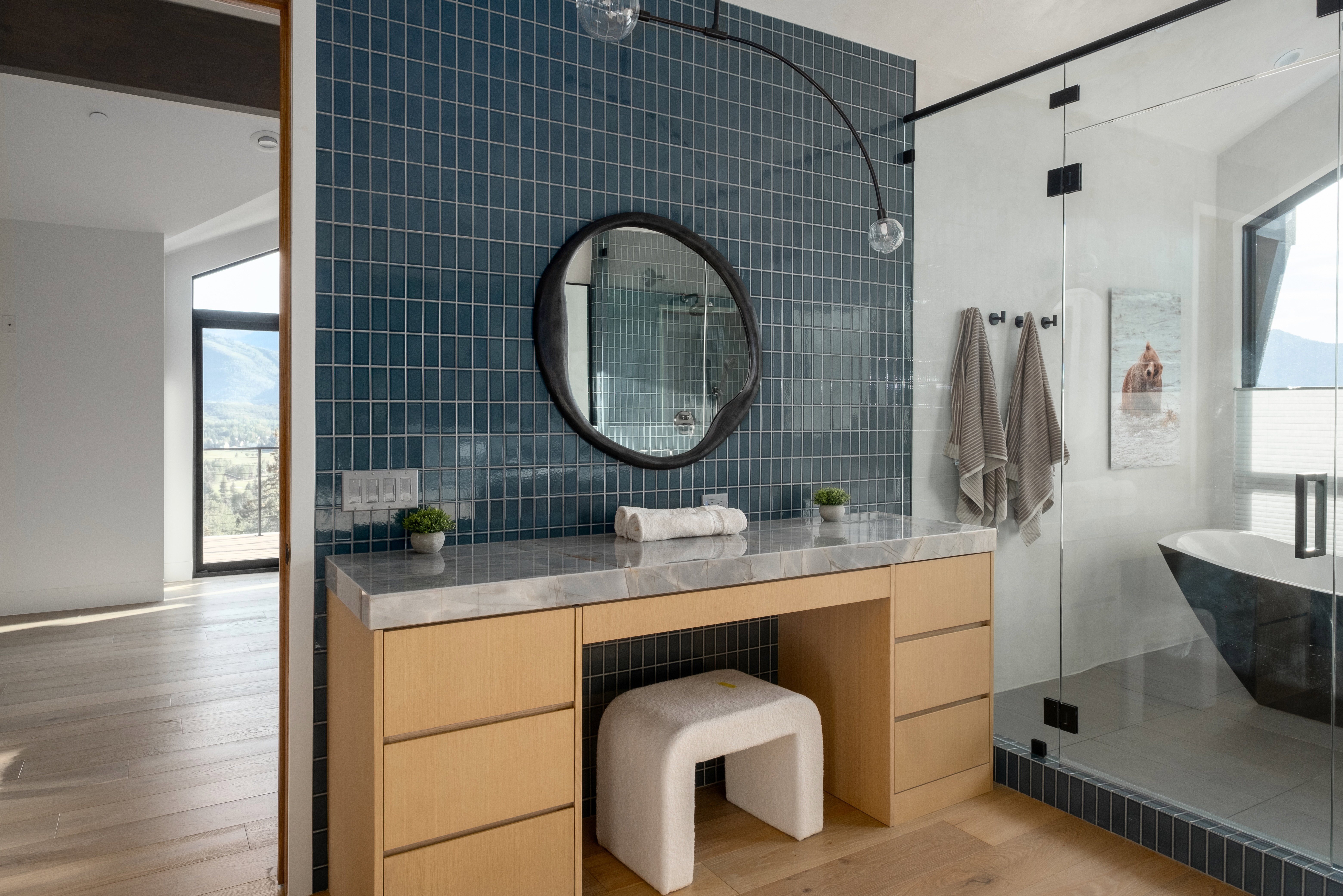 Bathroom vanity featuring a natural wood-finish base, stone countertop, and a circular mirror framed by a floor-to-ceiling blue tile accent wall