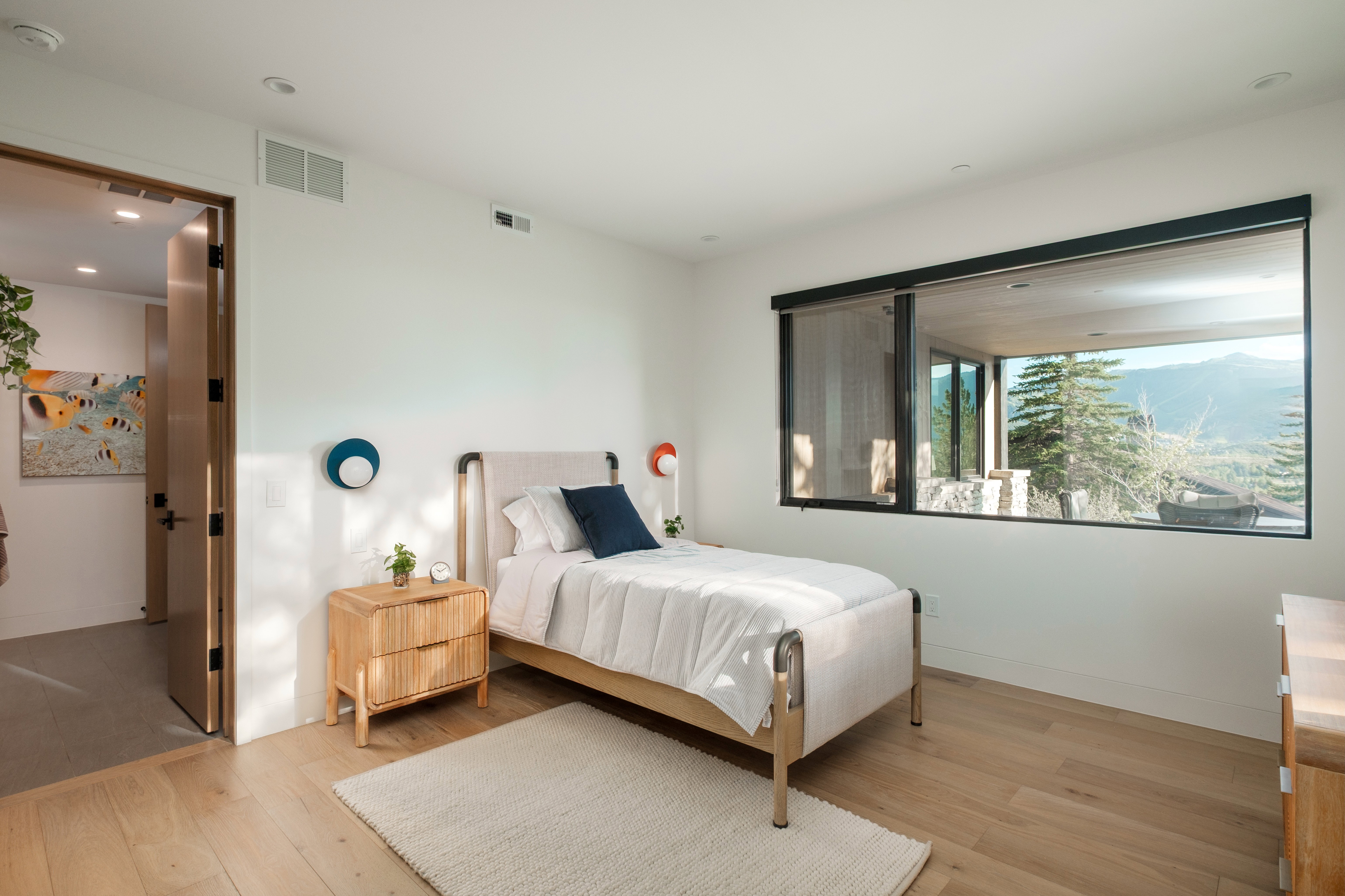 Bedroom featuring a large picture window, wood-finish flooring, white walls, and a light wood door with dark hardware