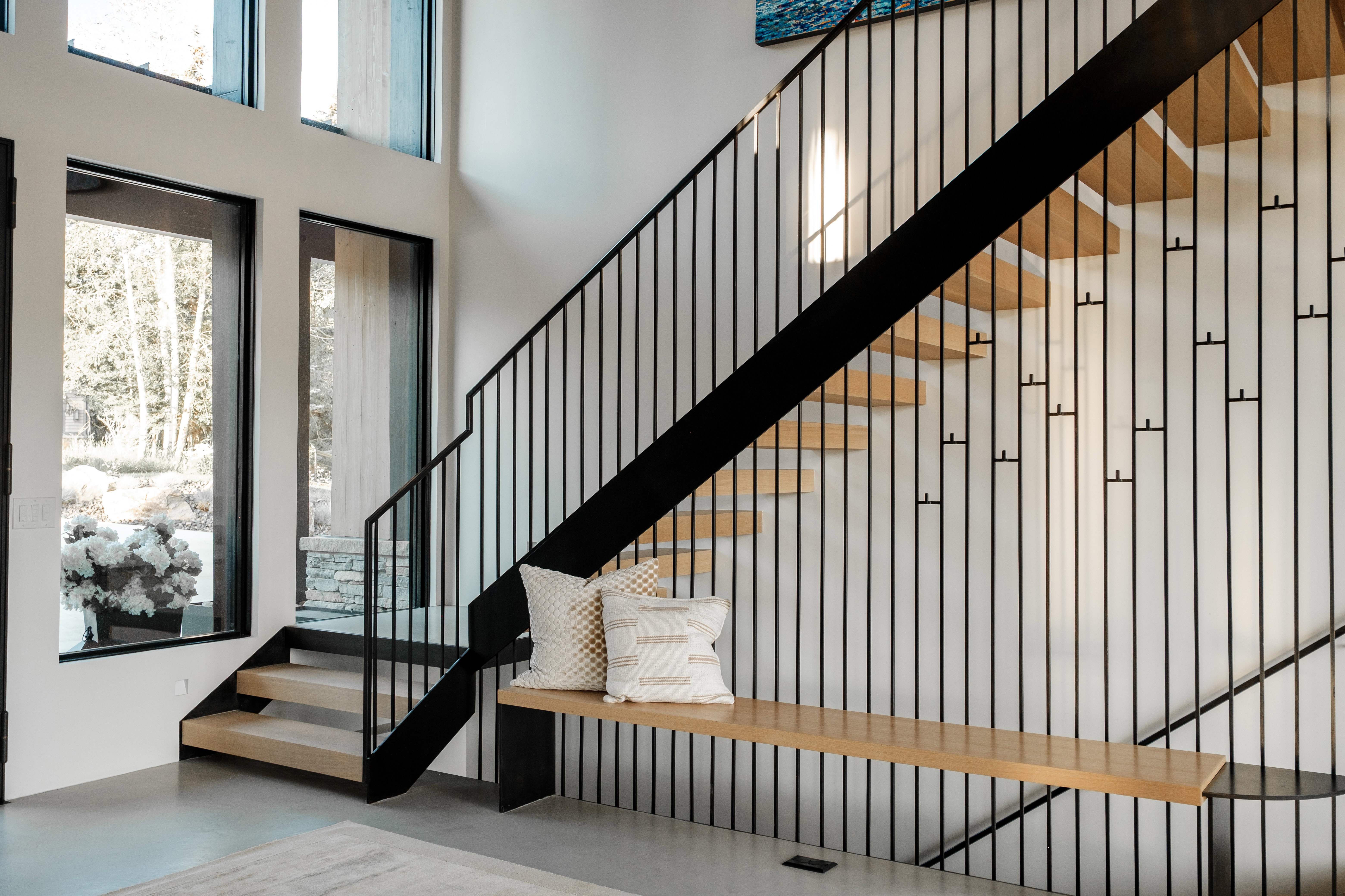 Modern staircase featuring a black metal railing with vertical spindles, light wood-finish treads, and an integrated wood-finish bench