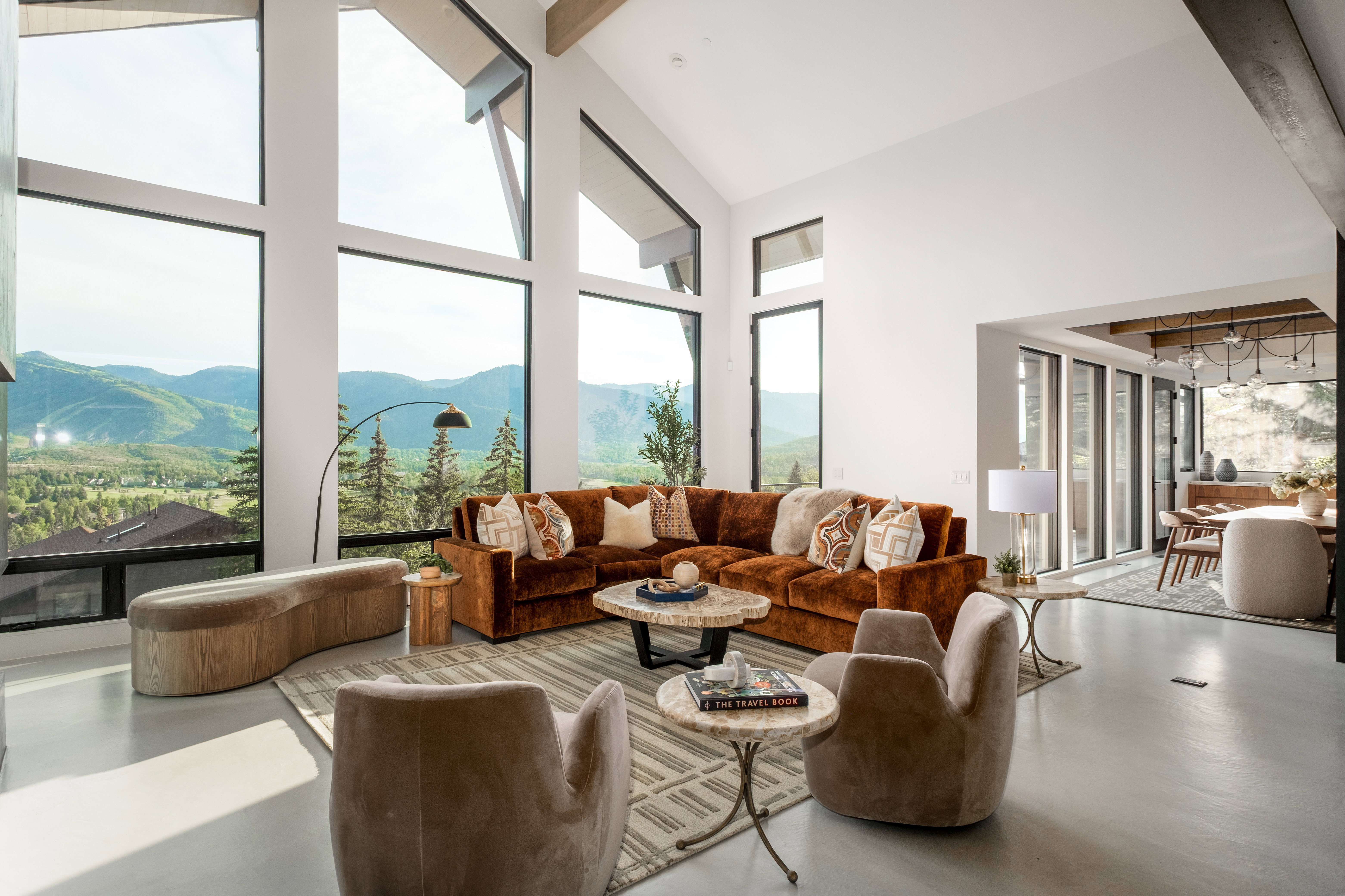Grand living space featuring expansive floor-to-ceiling windows, high vaulted ceilings with exposed beams, and polished concrete flooring