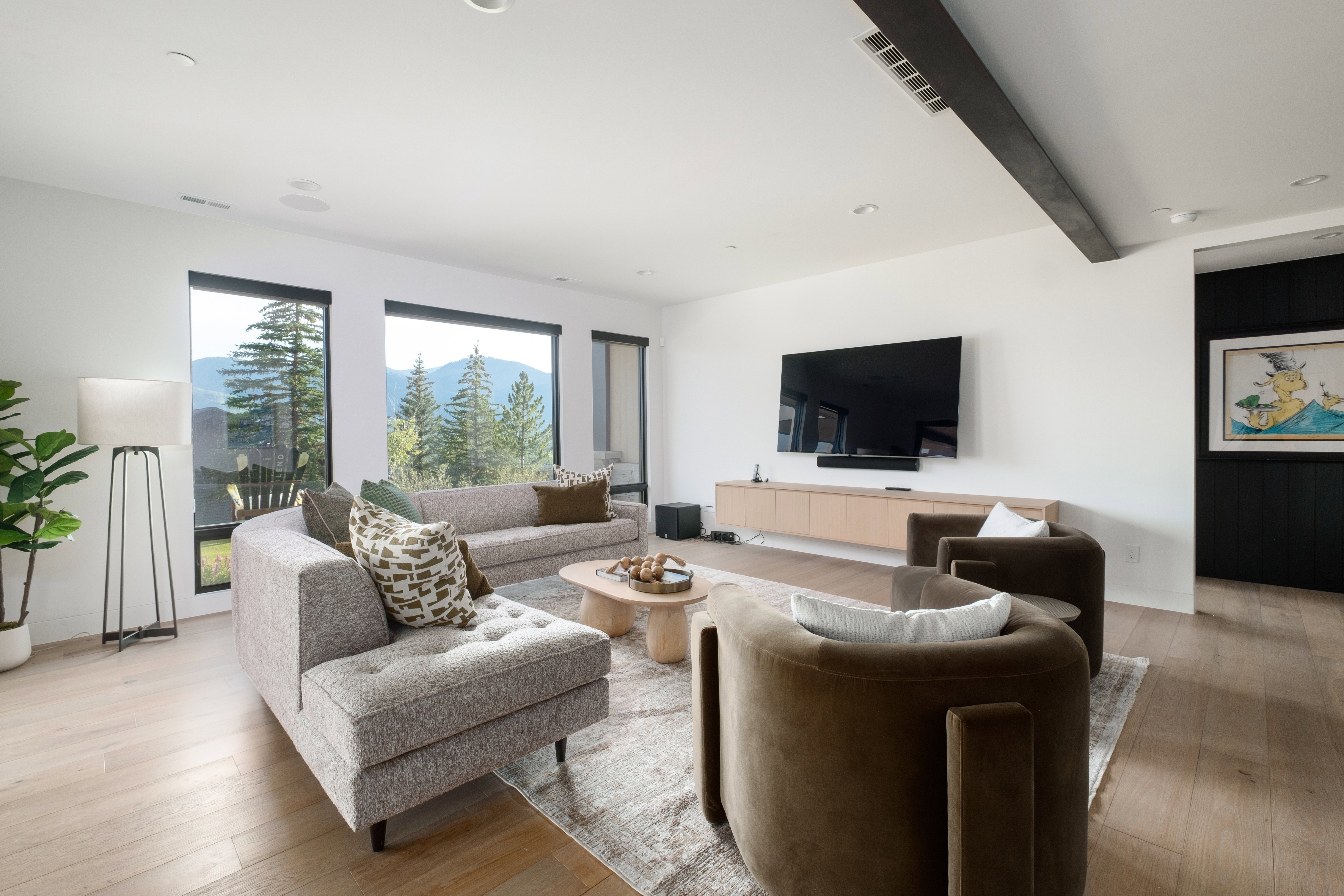 Spacious living area featuring large picture windows, wood-finish flooring, recessed lighting, and a prominent exposed ceiling beam