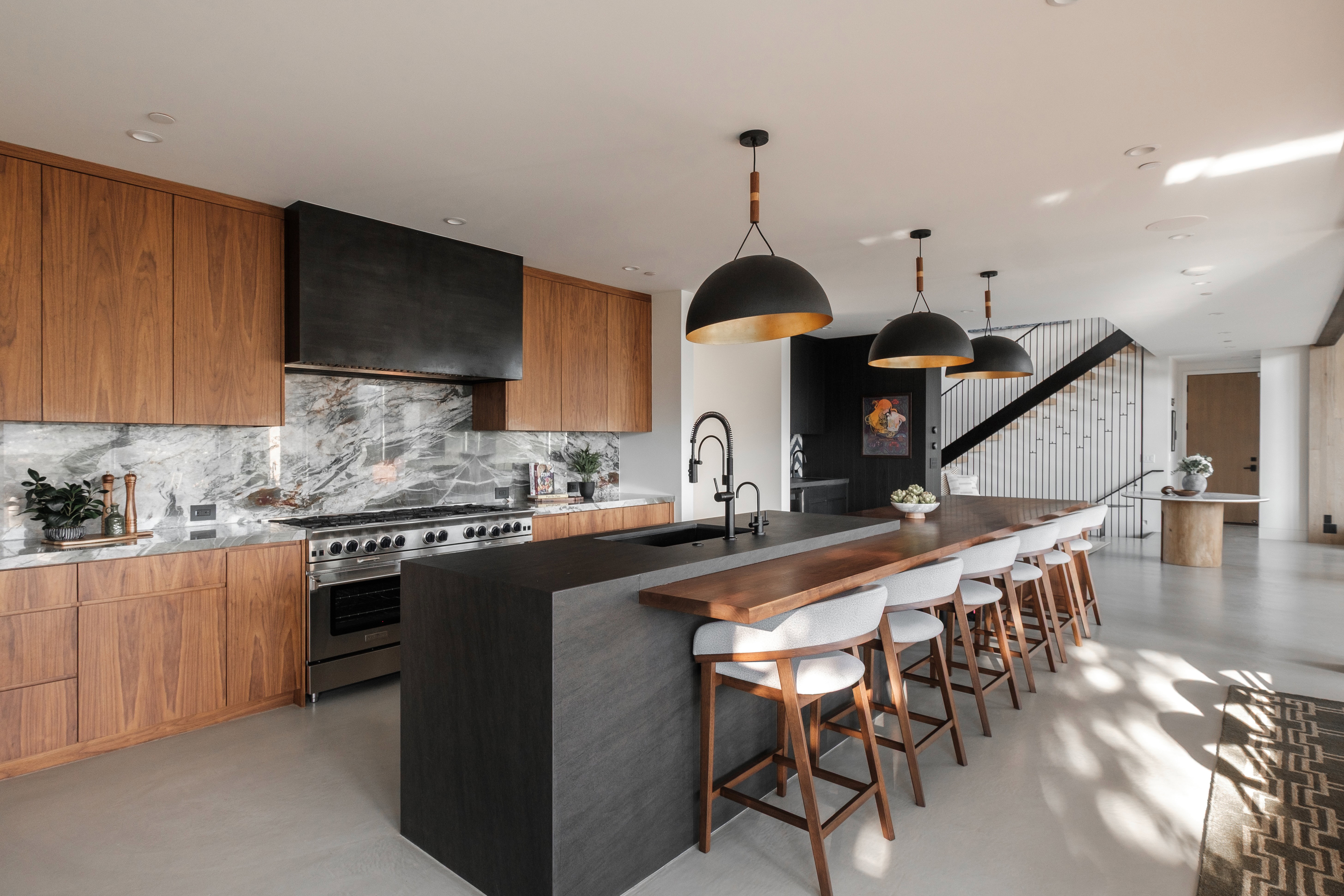 Spacious kitchen featuring custom wood cabinetry, a large center island with integrated wood-top seating, stainless steel professional-grade range, full marble slab backsplash, and contemporary pendant lighting