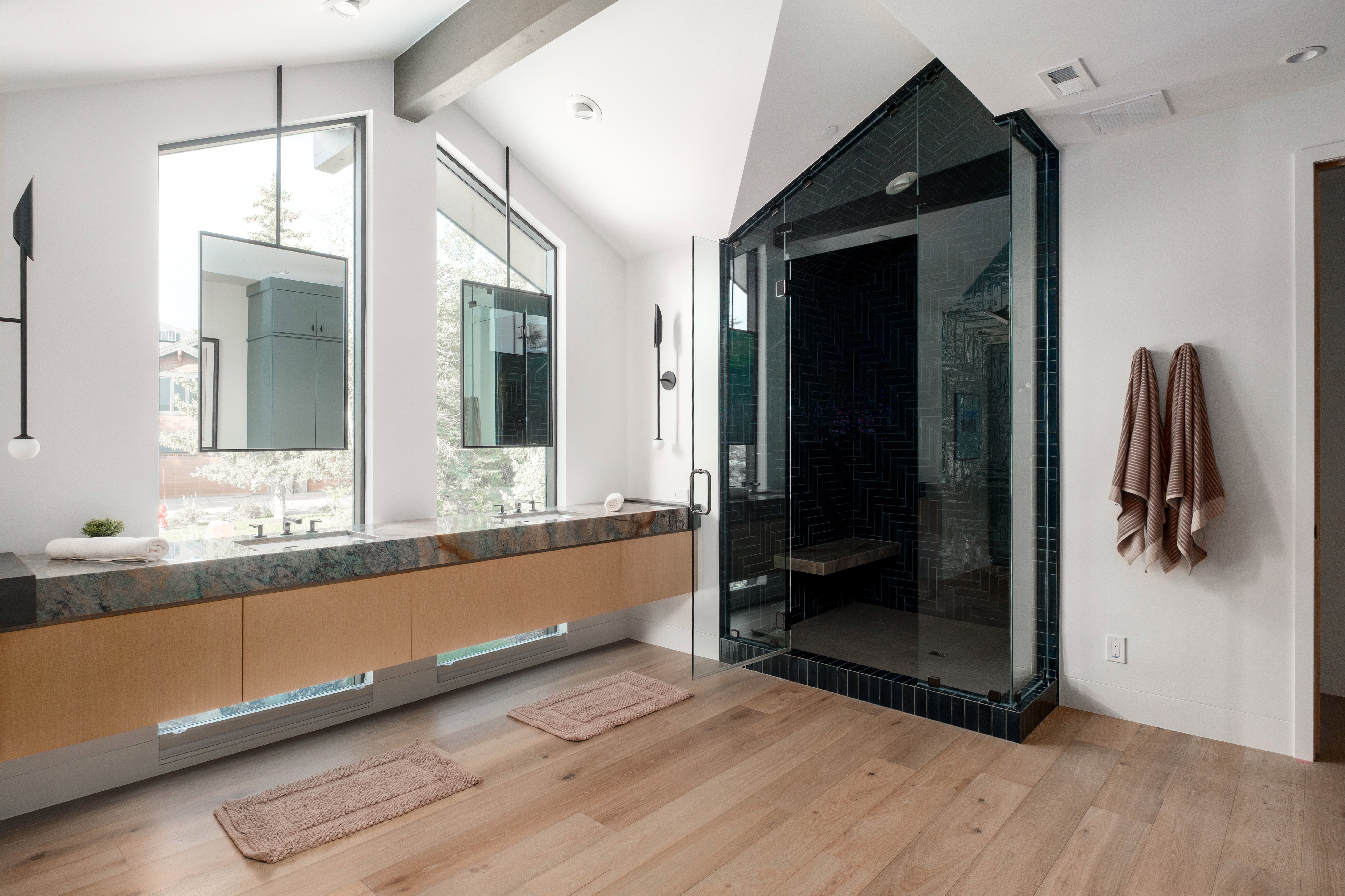 Modern bathroom featuring a double vanity with stone countertop, suspended mirrors, and pendant lighting