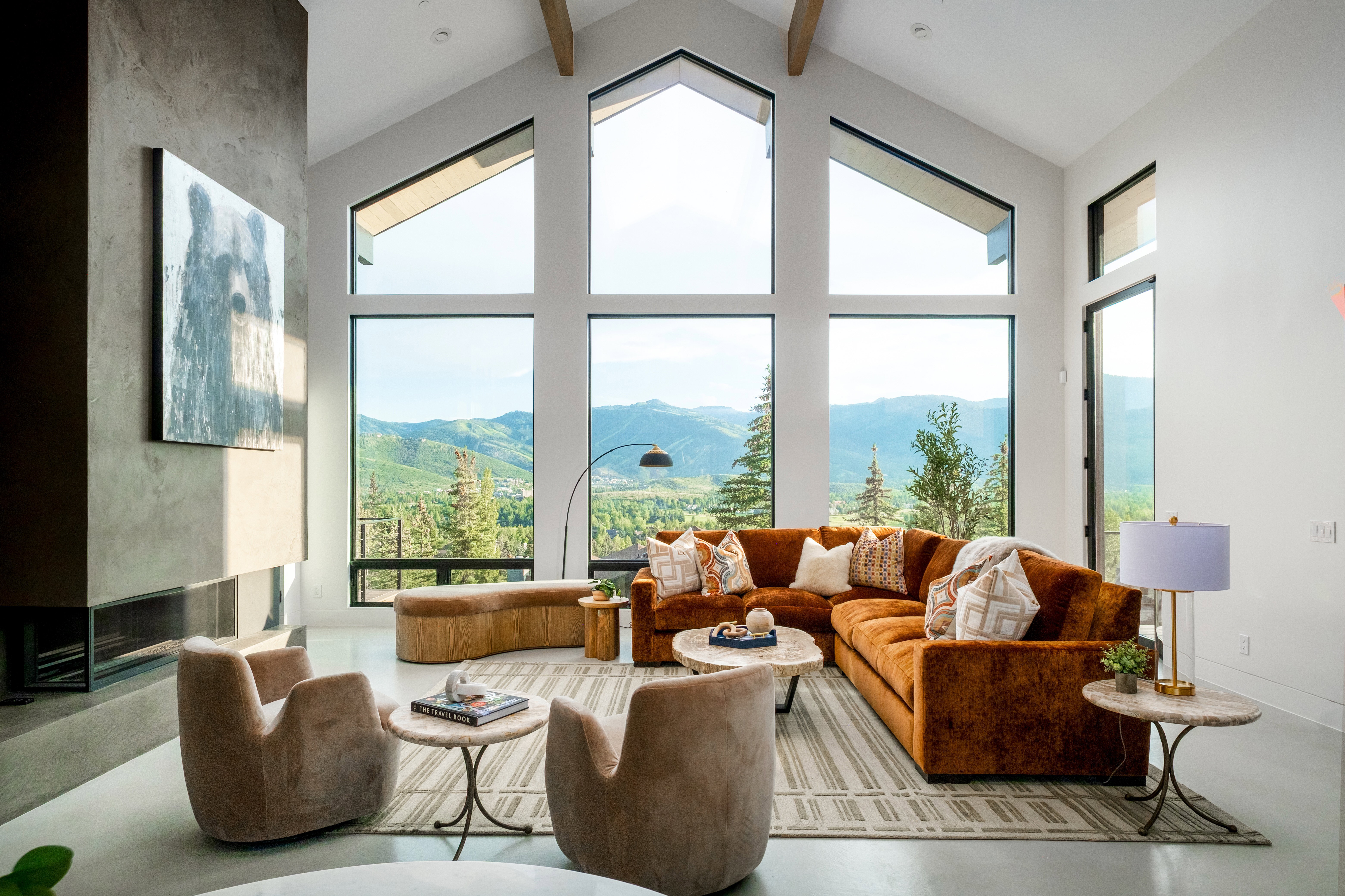 Vaulted ceilings with exposed beams, expansive floor-to-ceiling windows, and a built-in horizontal fireplace