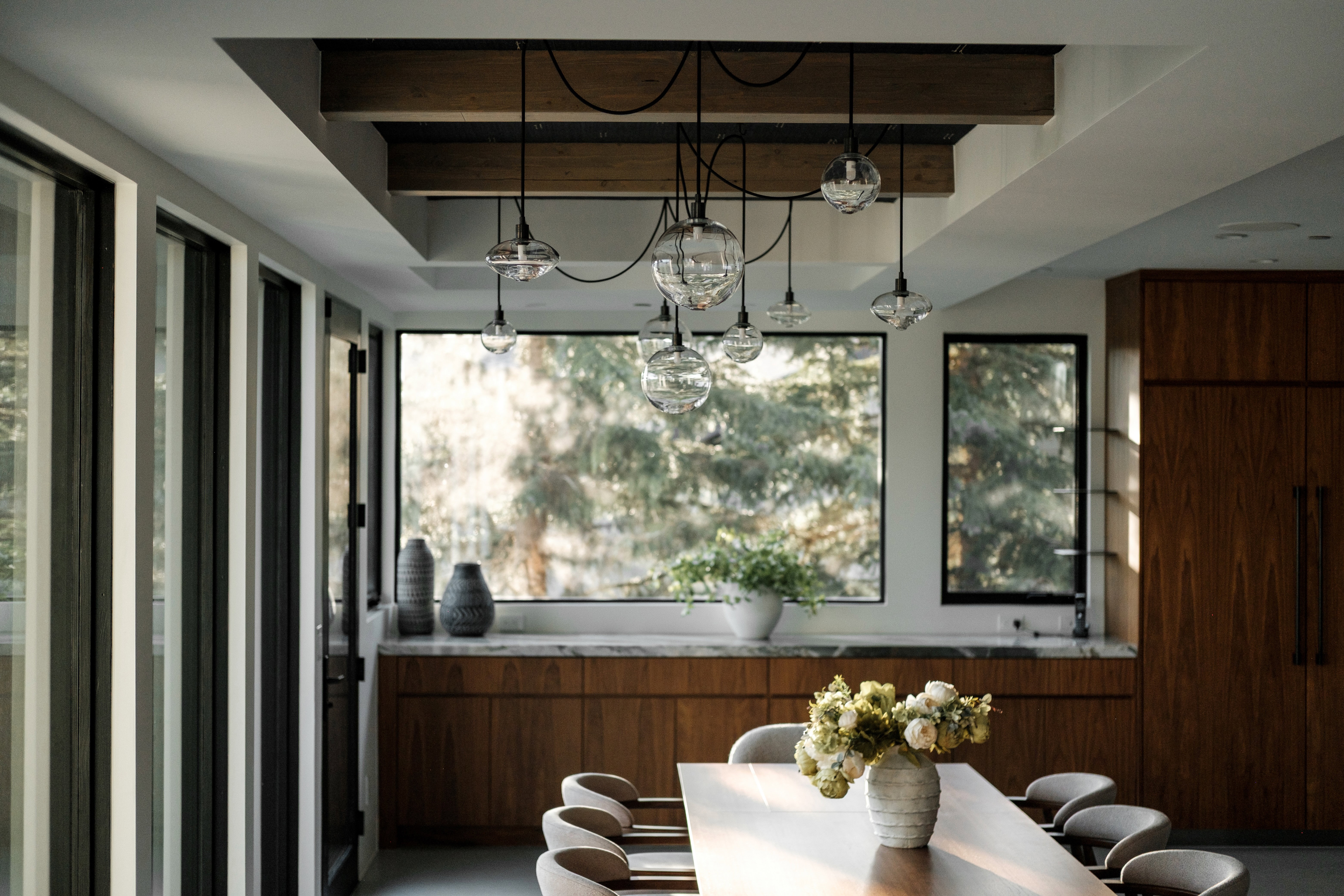 Dining area featuring a prominent wood beam ceiling detail, a multi-globe pendant light fixture, a wood-finish dining table, and built-in wood cabinetry with a light-toned countertop