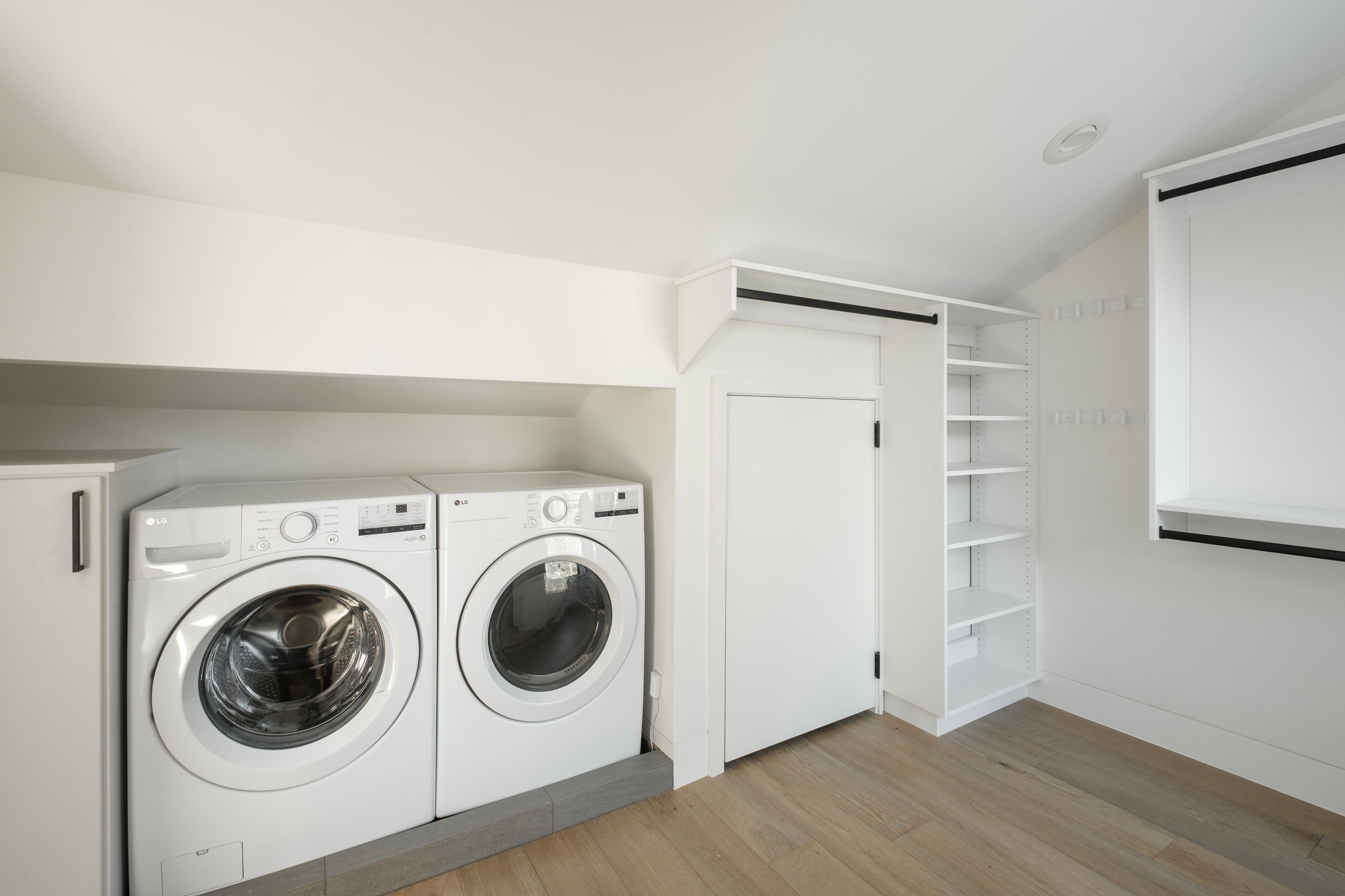 Dedicated laundry area featuring front-loading washer and dryer, wood-finish flooring, built-in shelving, white cabinetry, and recessed lighting