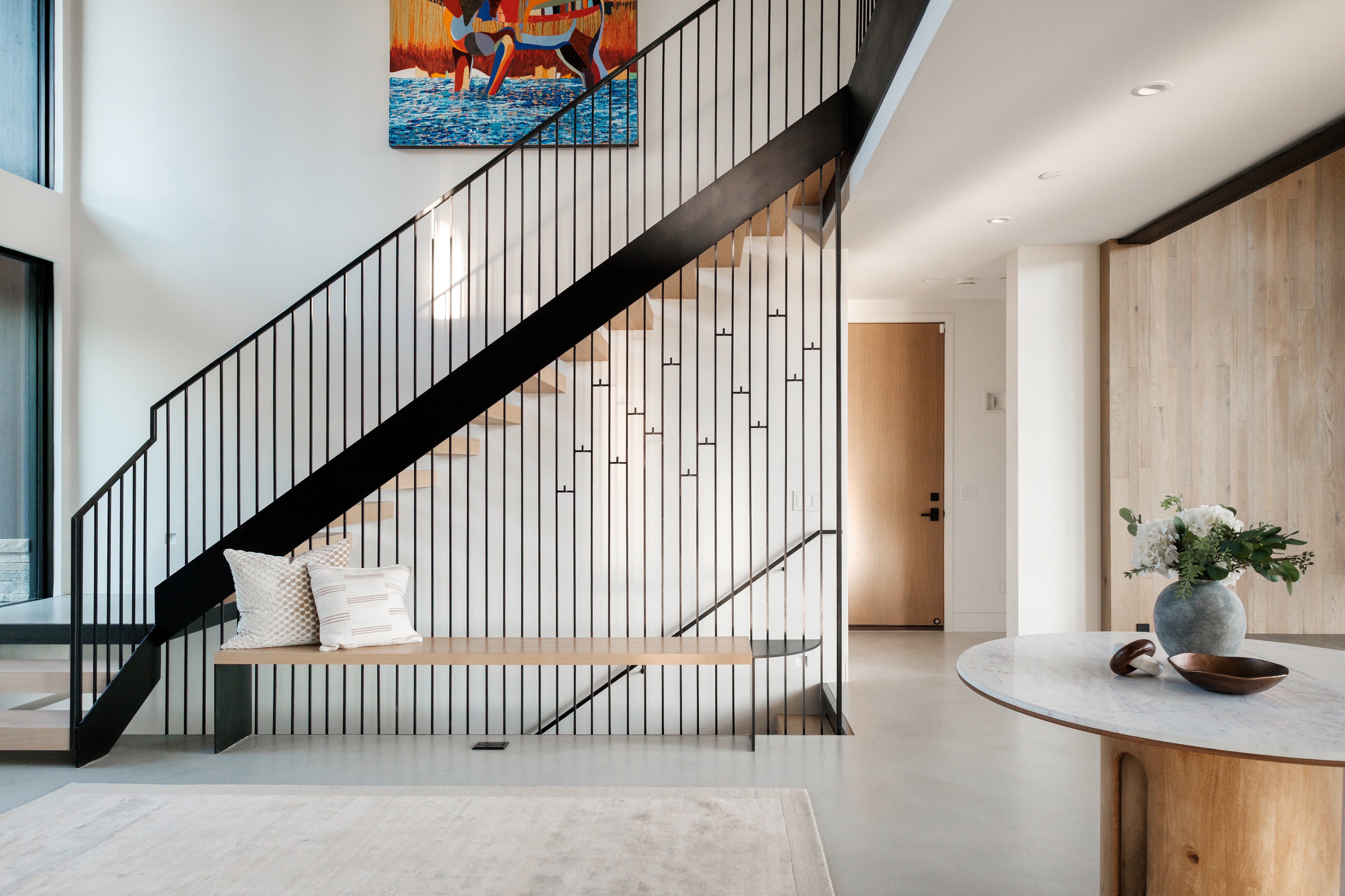 Staircase with modern black metal balusters, light wood-finish treads, and integrated light wood bench seating