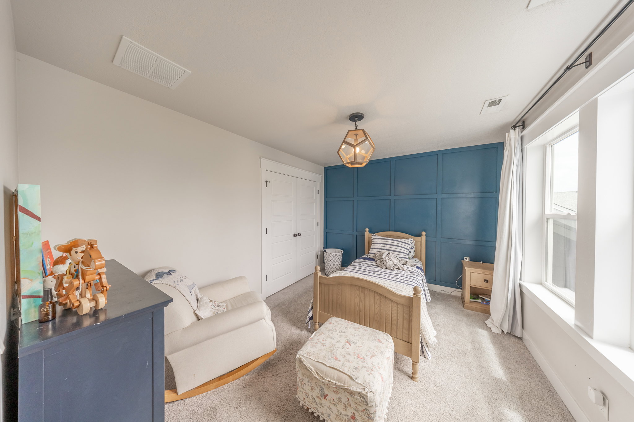 Bedroom featuring a paneled accent wall, neutral carpeting, and a geometric pendant light fixture