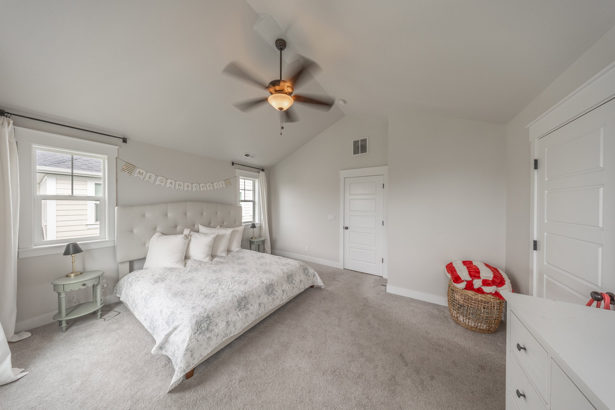 Spacious bedroom featuring vaulted ceilings, plush carpeting, two windows with white trim, and a ceiling fan with integrated lighting