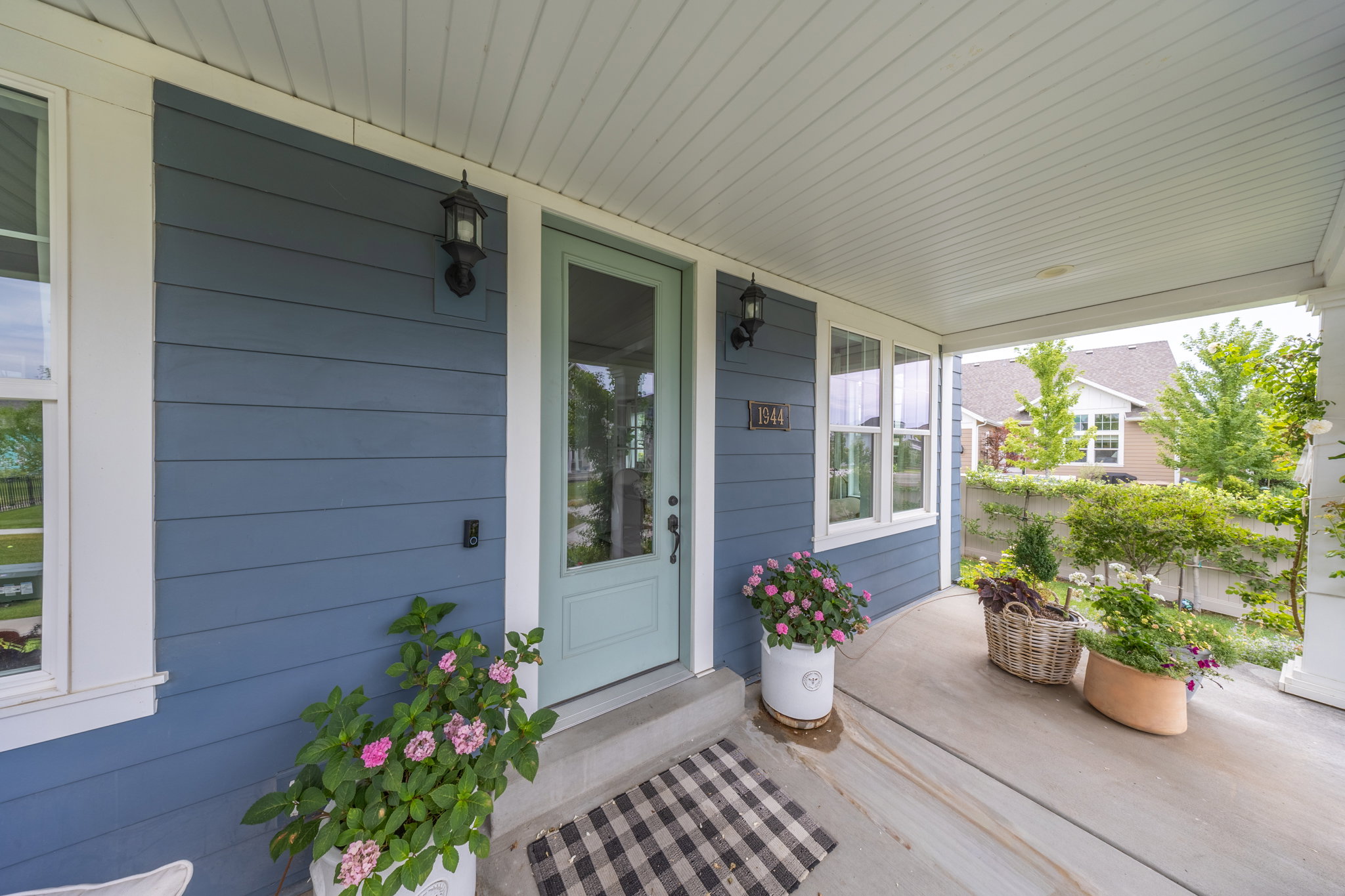Covered front porch featuring blue horizontal siding, white trim, a light aqua door, and exterior sconce lighting