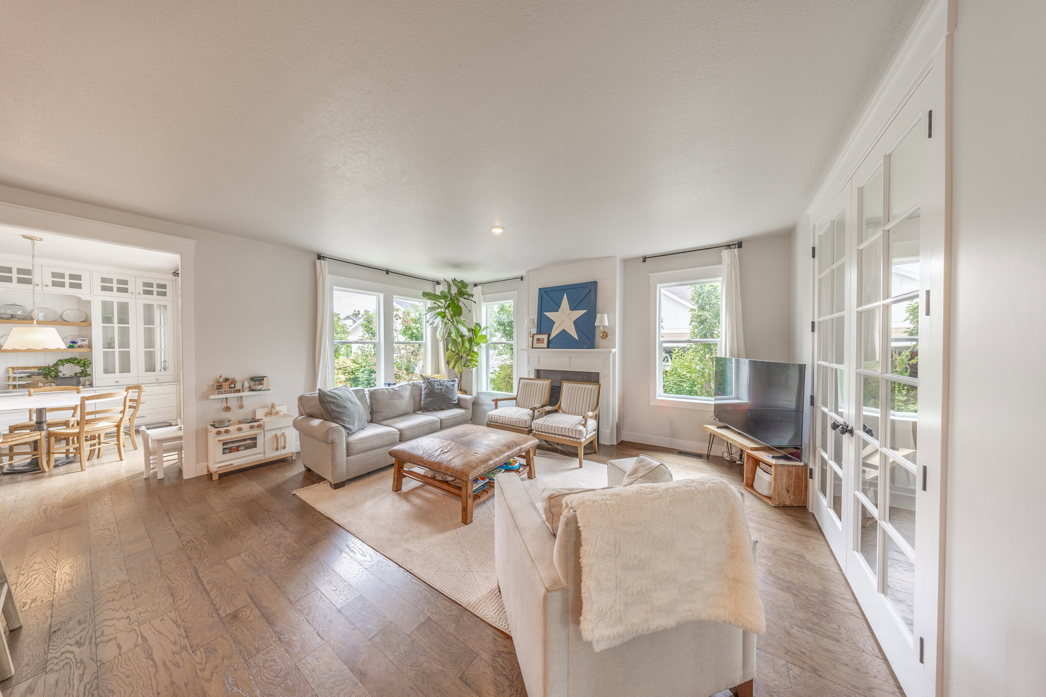 Spacious living area featuring wood-finish flooring, a white fireplace with a mantel, multiple windows, and French doors