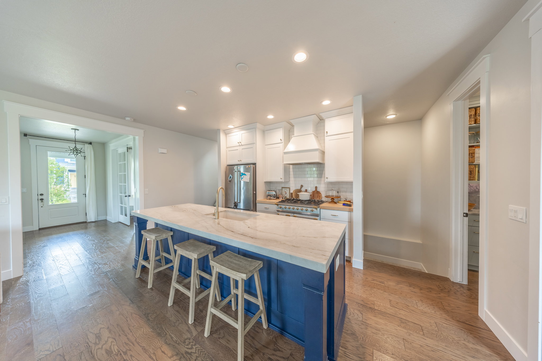 Kitchen featuring a large island with stone countertop, stainless steel appliances, white cabinetry, and wood-finish flooring