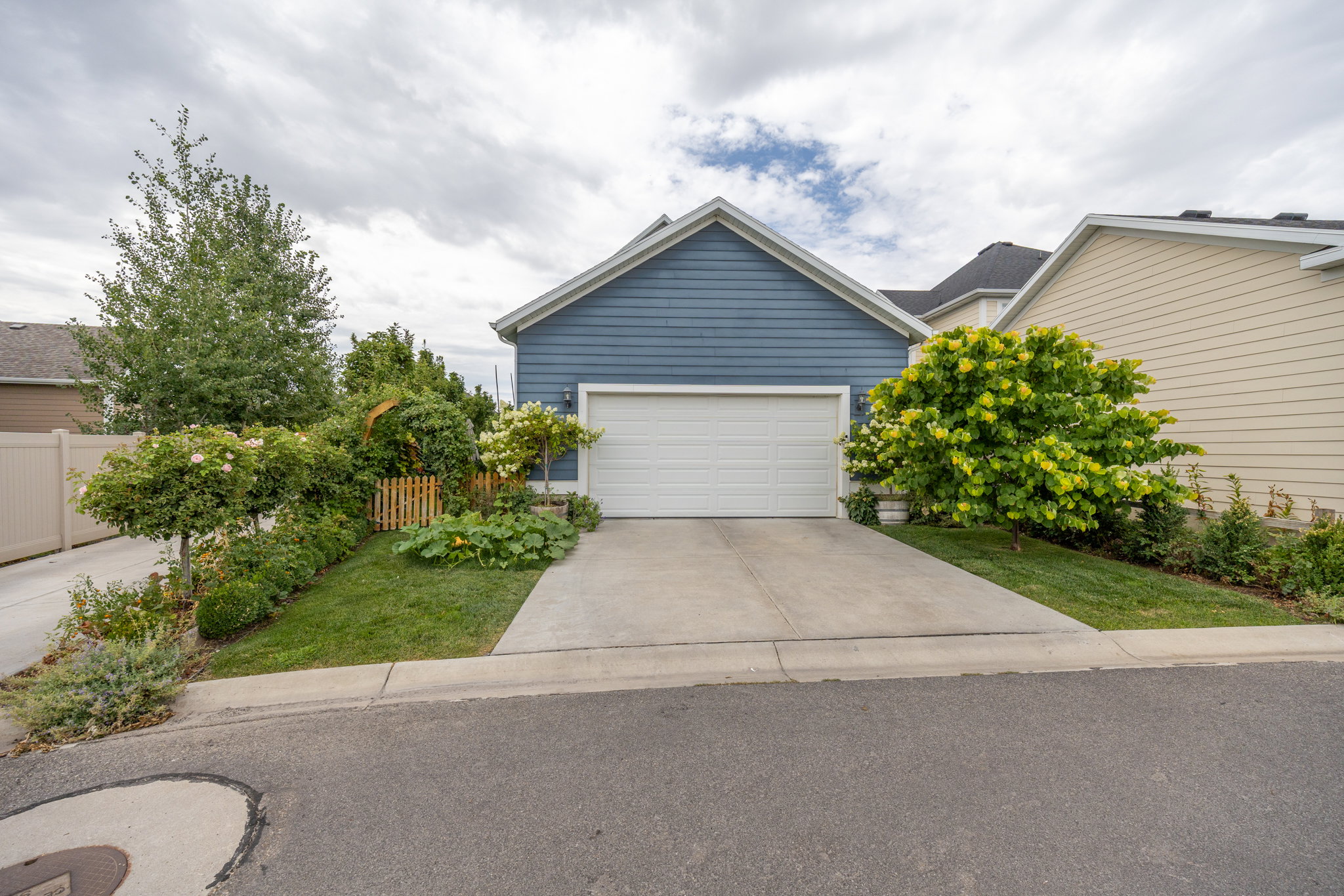 Blue horizontal siding exterior with white garage door, concrete driveway, and established front yard landscaping