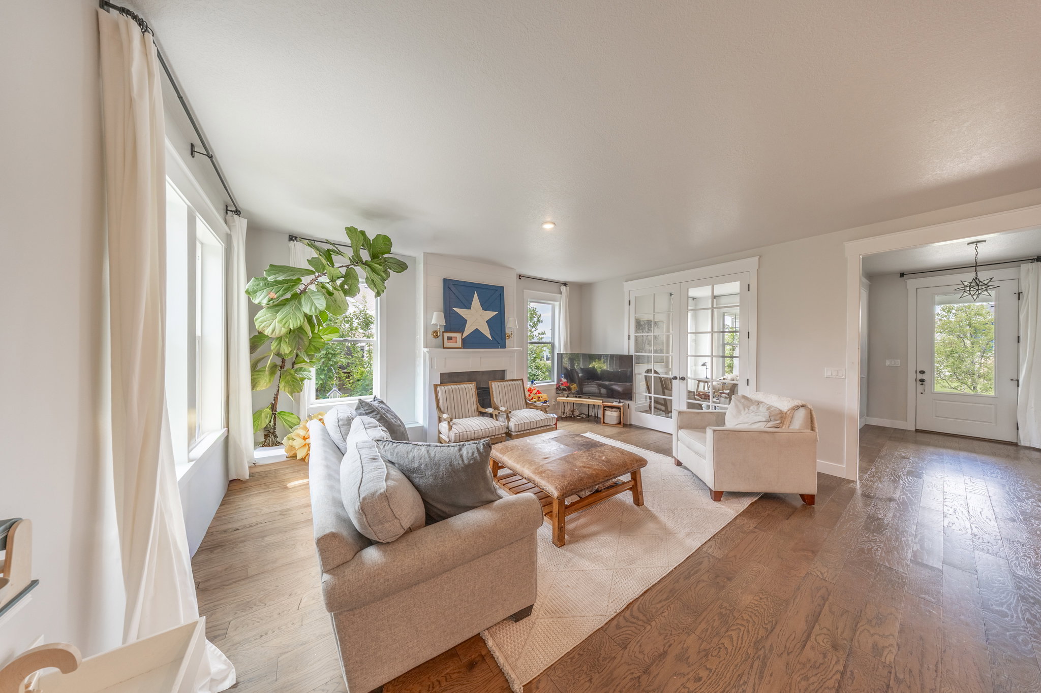 Spacious living area featuring wood-finish flooring, a fireplace with mantel, and white-framed windows