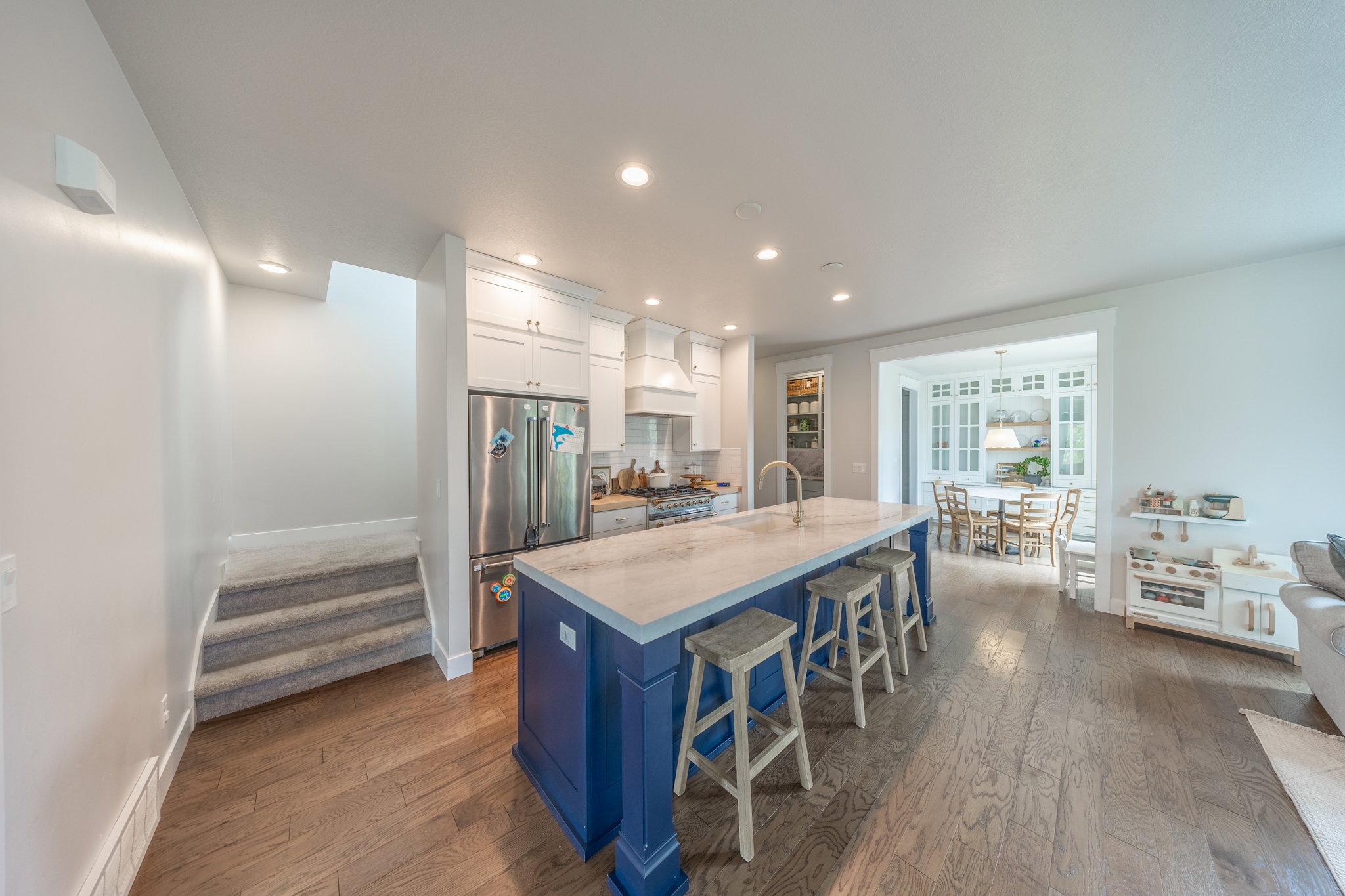 Kitchen featuring a blue island with light-toned countertop, stainless steel refrigerator, white cabinetry, and wood-finish flooring