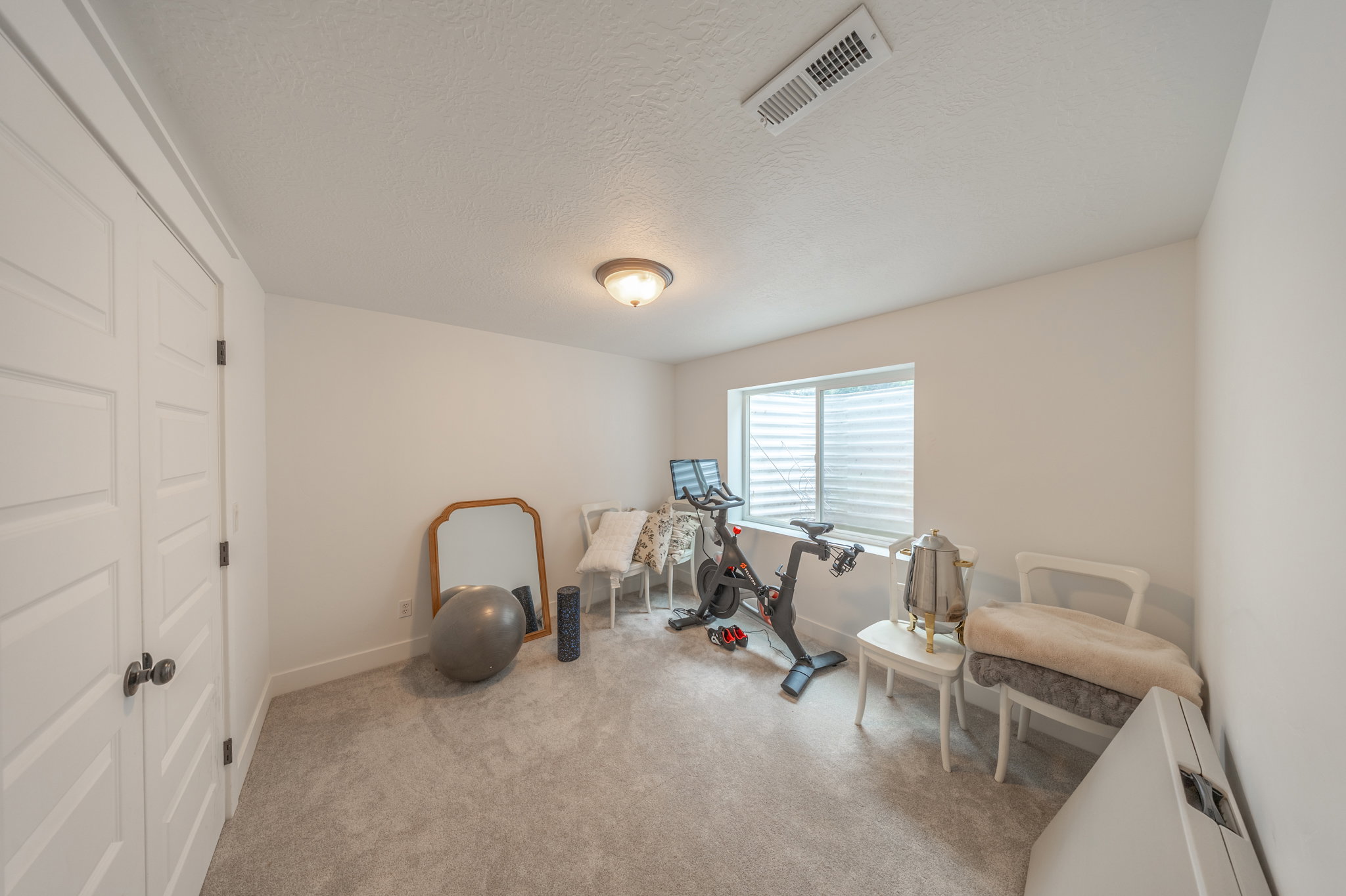 Carpeted room featuring a ceiling-mounted light fixture, white walls, and a window with blinds