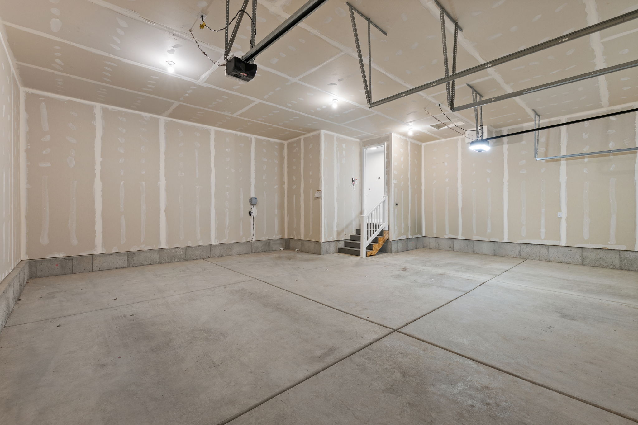 Spacious garage featuring a concrete floor, overhead lighting, garage door opener, and interior stairs with a white railing