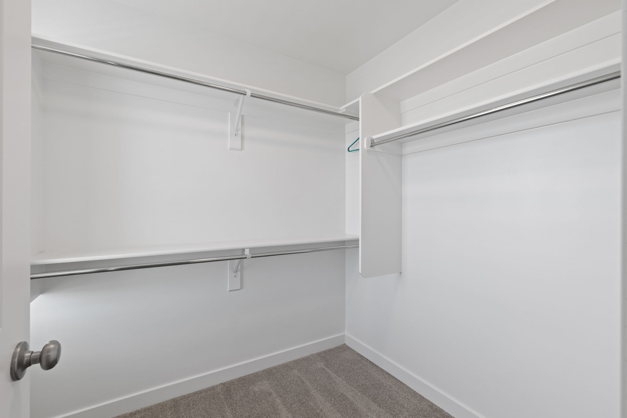 Spacious walk-in closet featuring white shelving and chrome hanging rods
