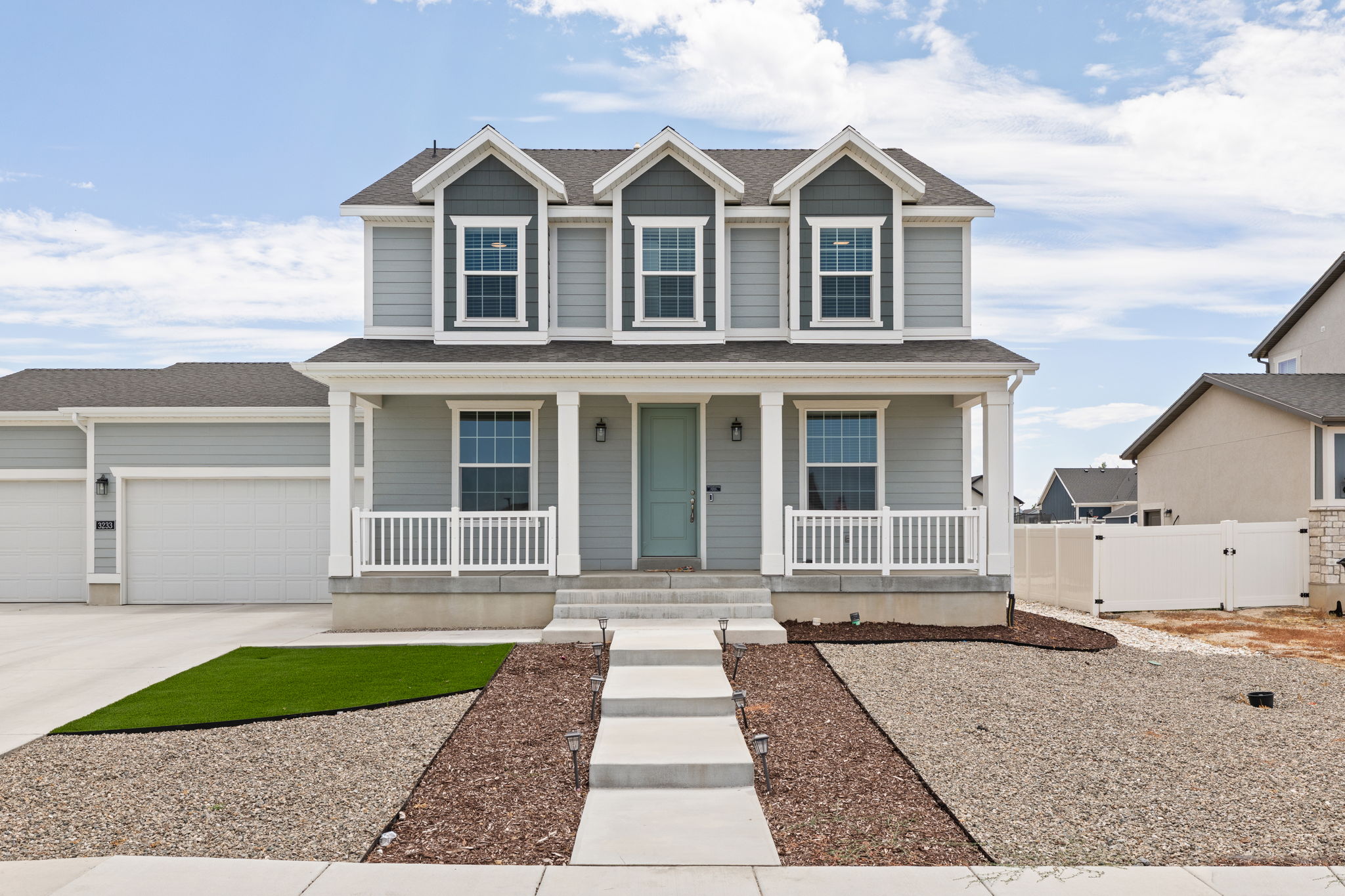 Two-story residence featuring light gray siding with dark gray gables, a covered front porch with white railings, and a light-colored front door