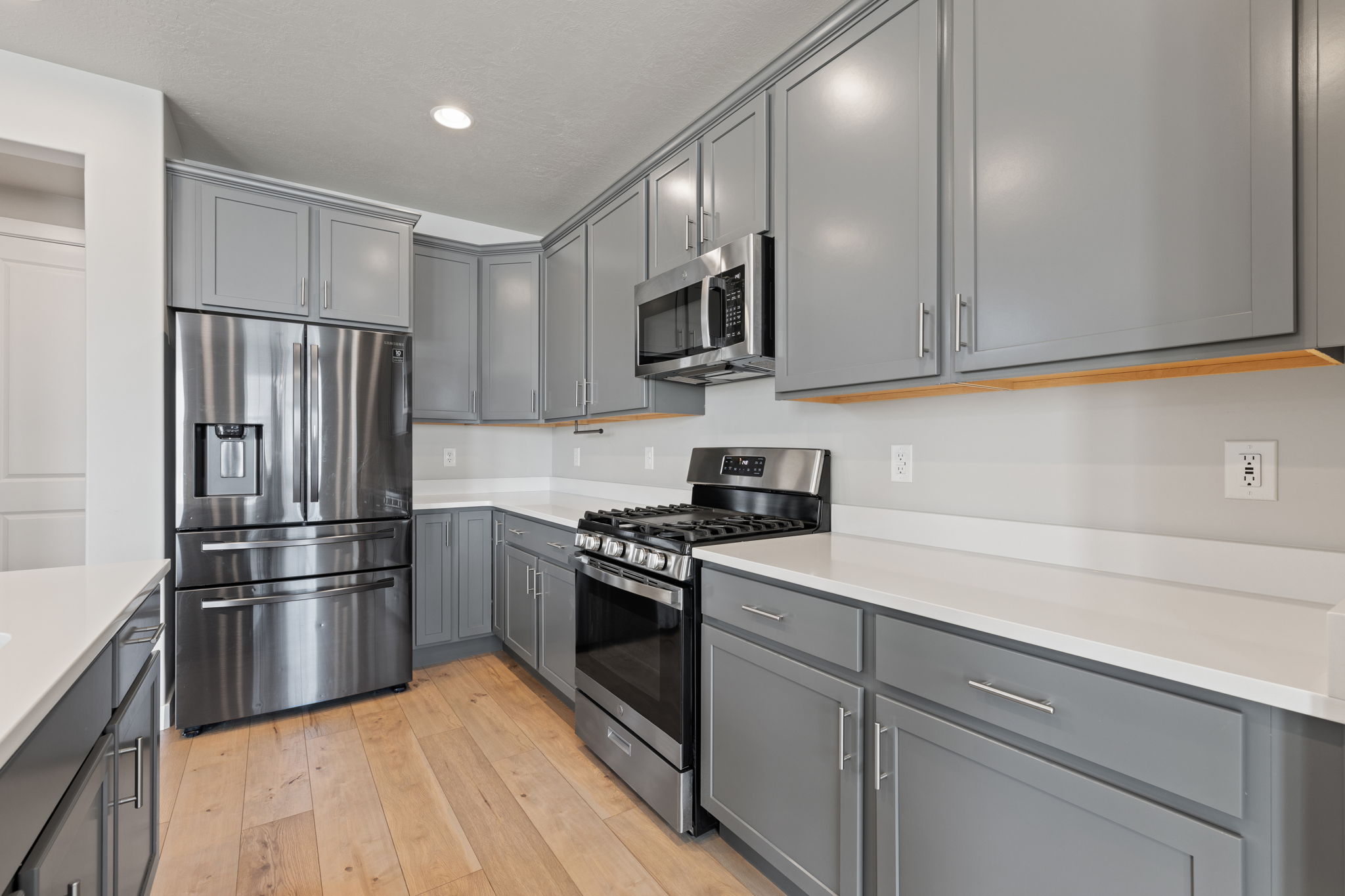 Contemporary kitchen featuring light wood-finish flooring, gray cabinetry, white countertops, and stainless steel appliances including a gas range and French door refrigerator