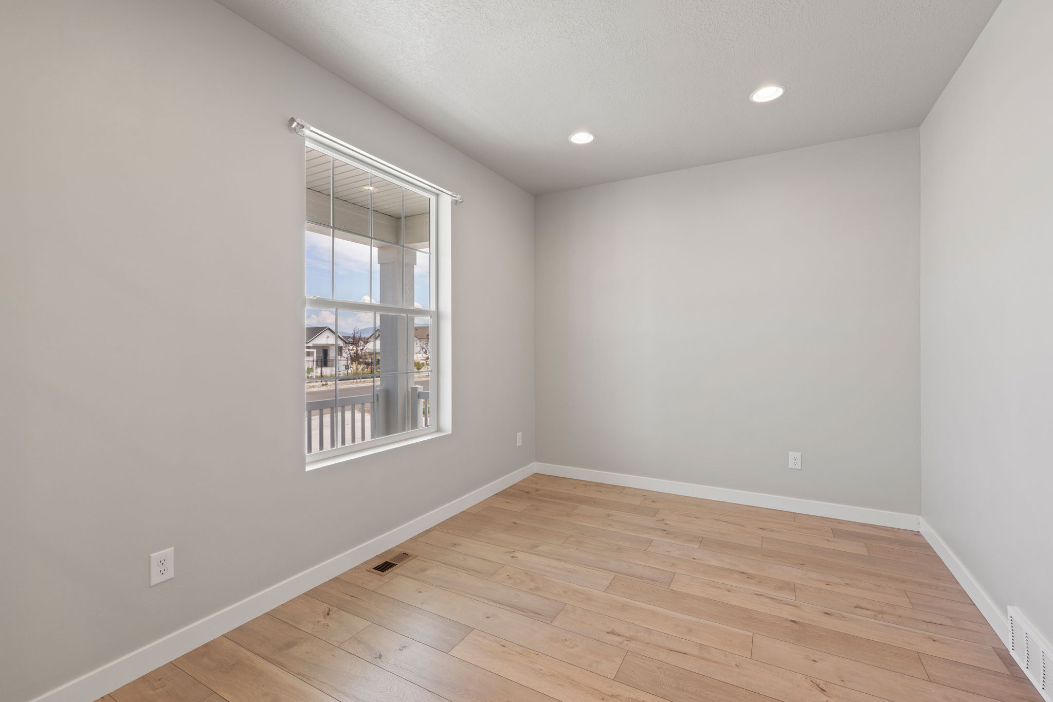 Light-filled room featuring wood-finish flooring, recessed lighting, a double-hung window, and neutral wall tones